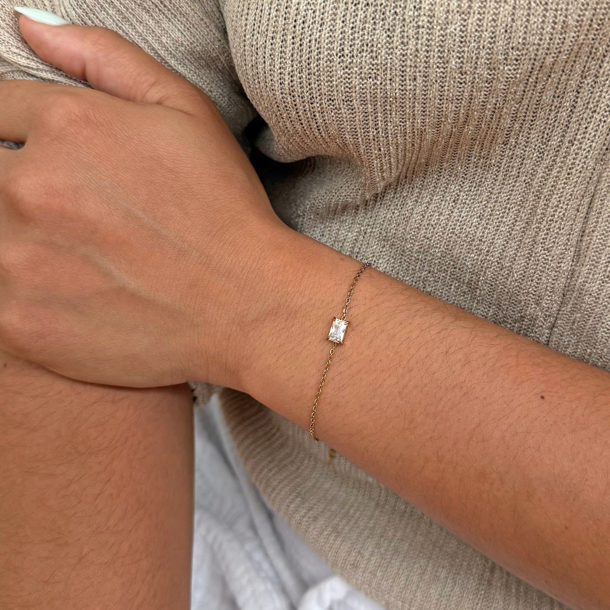 Close-up of a hand wearing a gold bracelet with a diamond on a neutral background