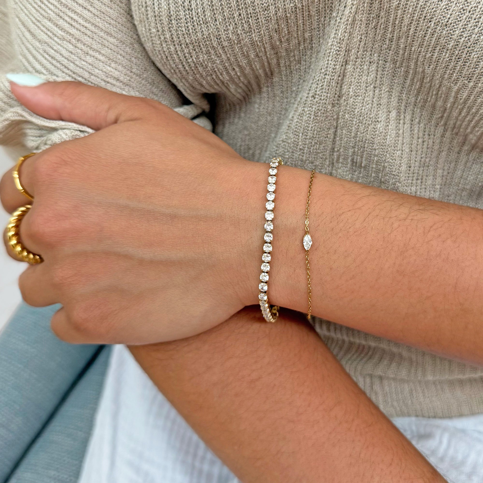 Close-up of a hand wearing gold dainty marquis stone bracelet stacked with tennis bracelet waterproof jewelry