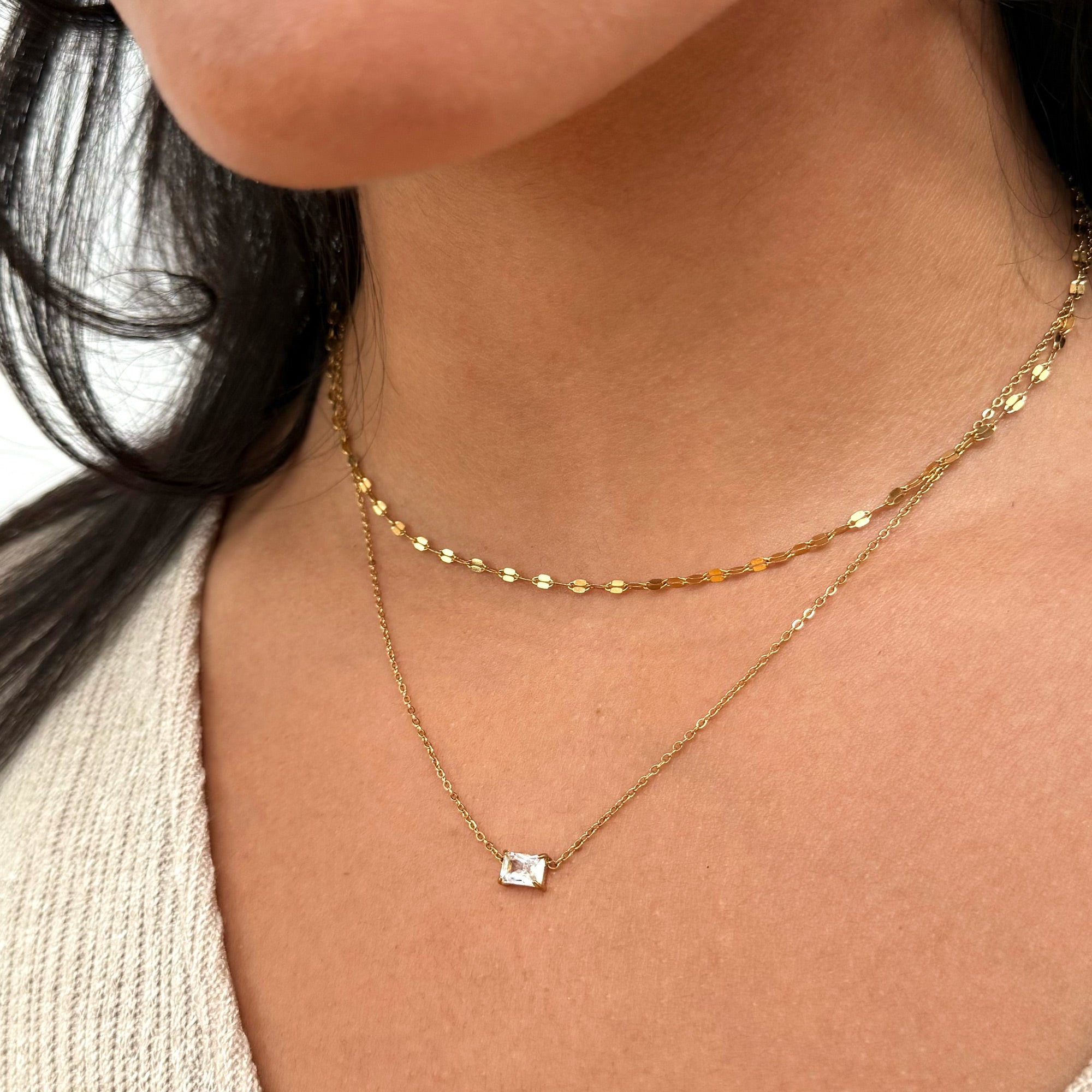 Close-up of a person wearing a gold necklace with a small emerald cut pendant waterproof jewelry