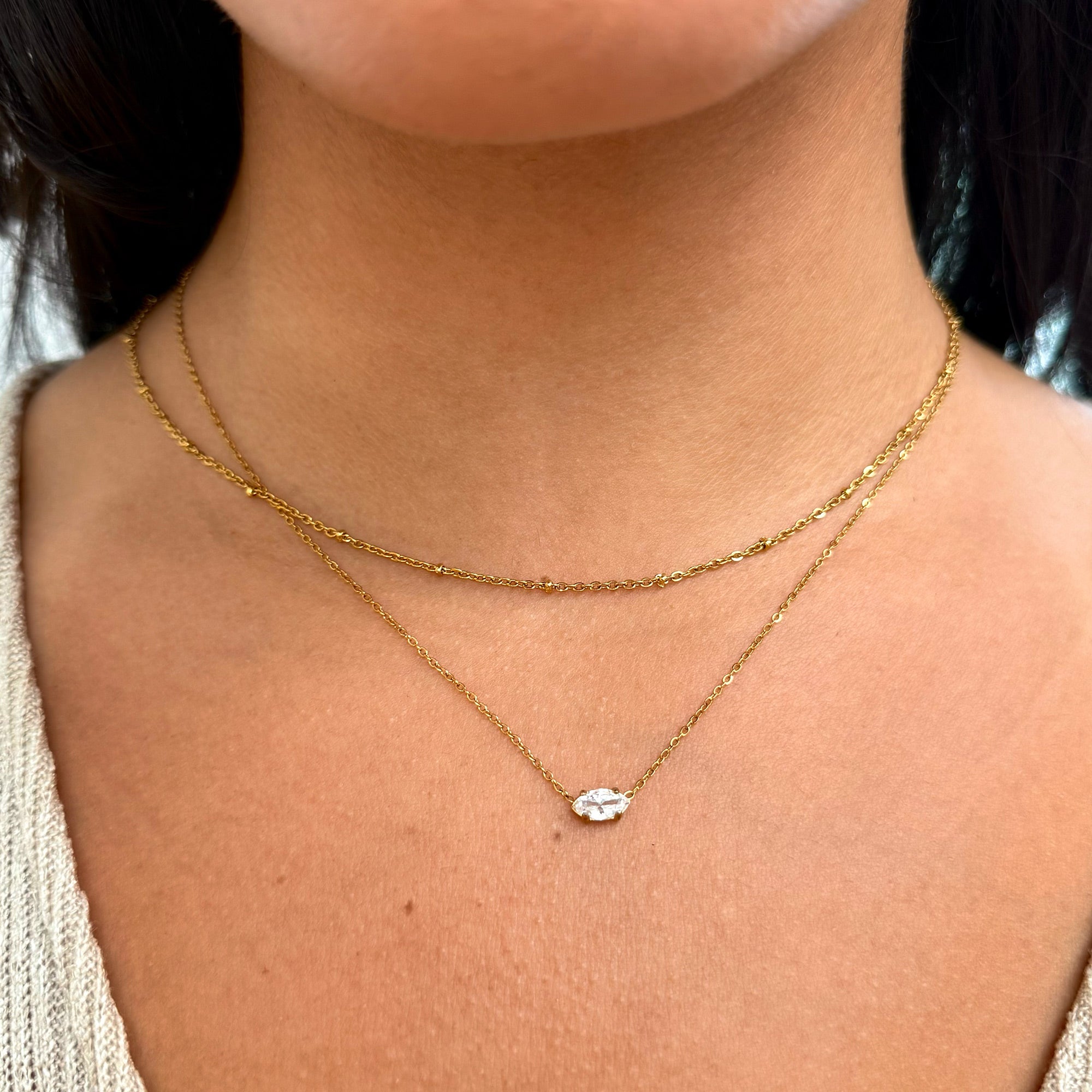 Close-up of a person wearing a dainty gold chain stacked with a small marquis pendant waterproof jewelry