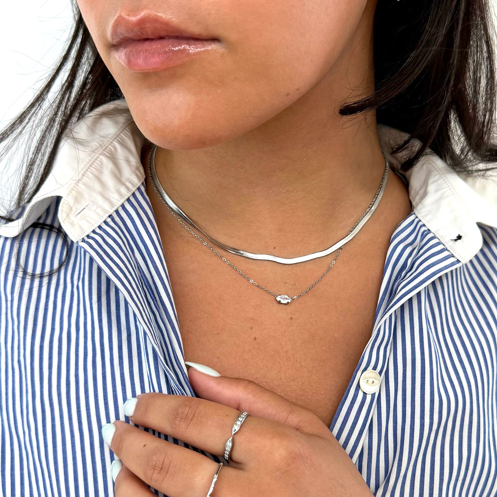 Close-up of a person wearing a dainty silver marquis stone necklace and ring, with a blue and white striped shirt. Tarnish free jewelry