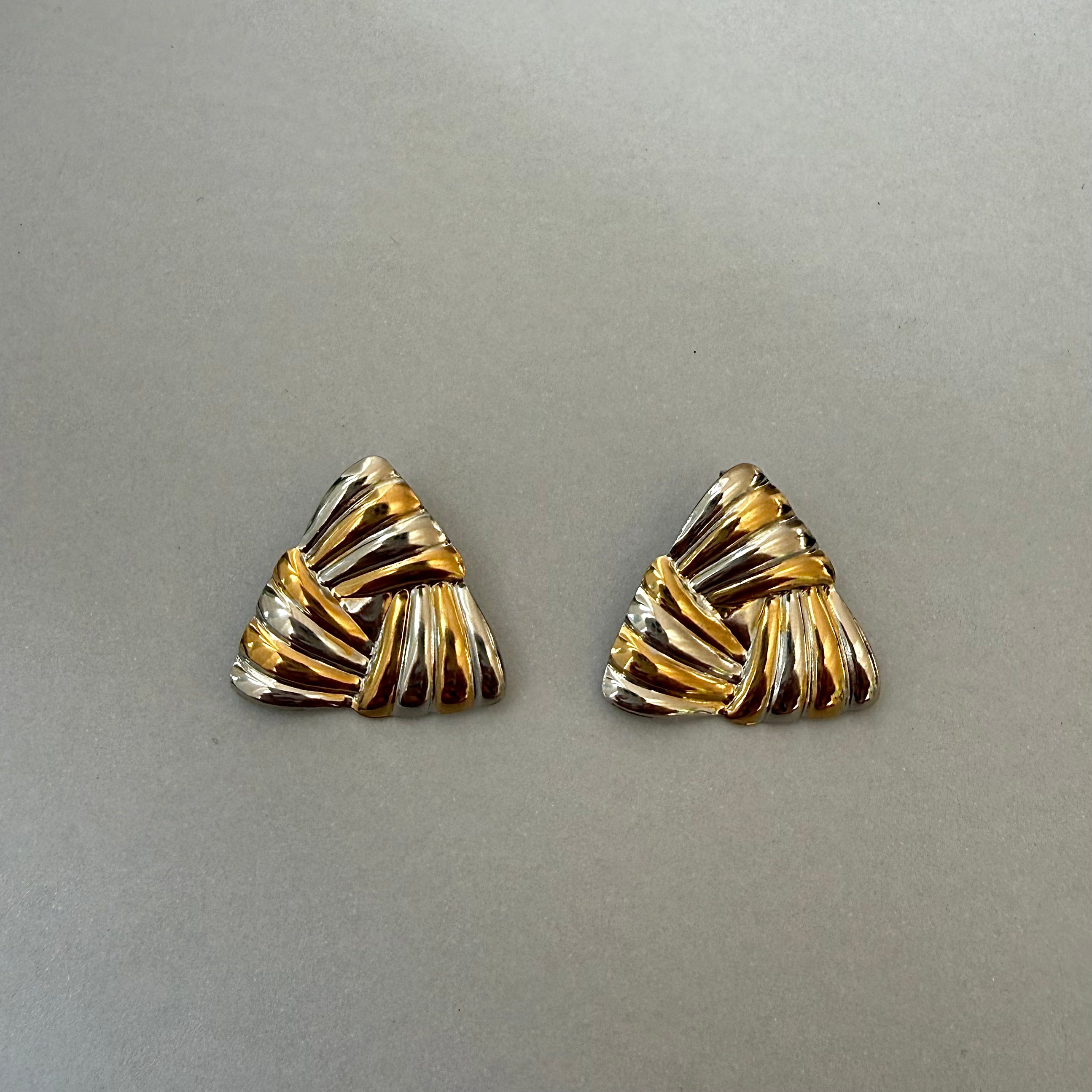 Pair of gold and silver triangle-shaped earrings on a gray background