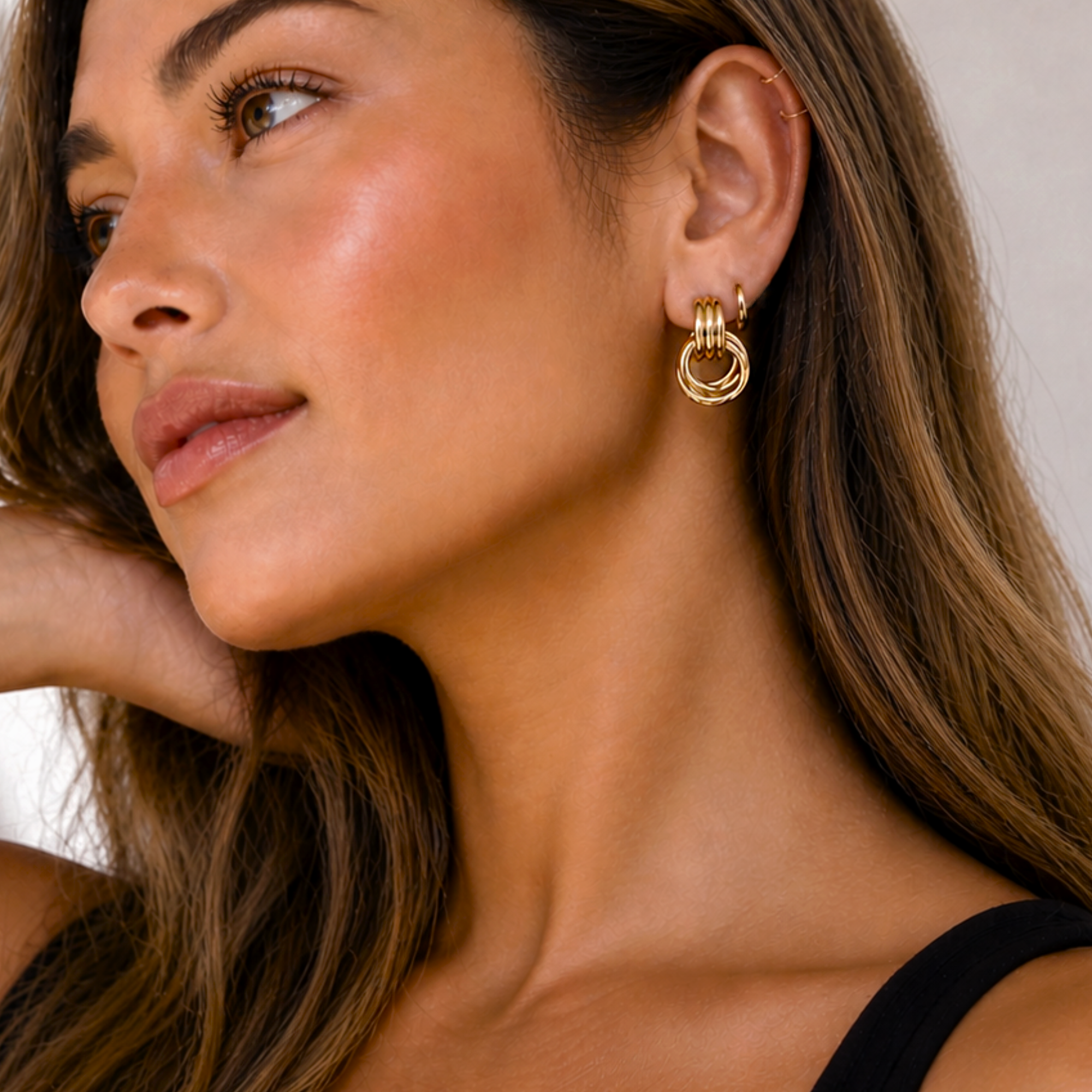 Close-up of a woman wearing gold door knocker hoop earrings with a neutral background