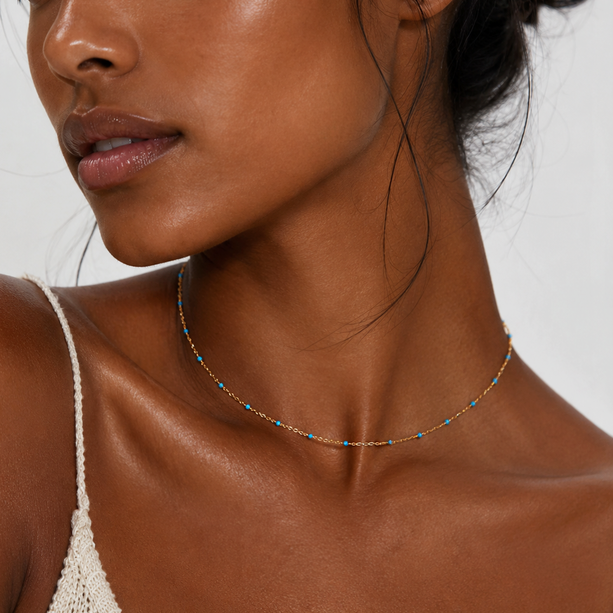 Close-up of a woman wearing a dainty blue beaded gold delicate necklace with a neutral background