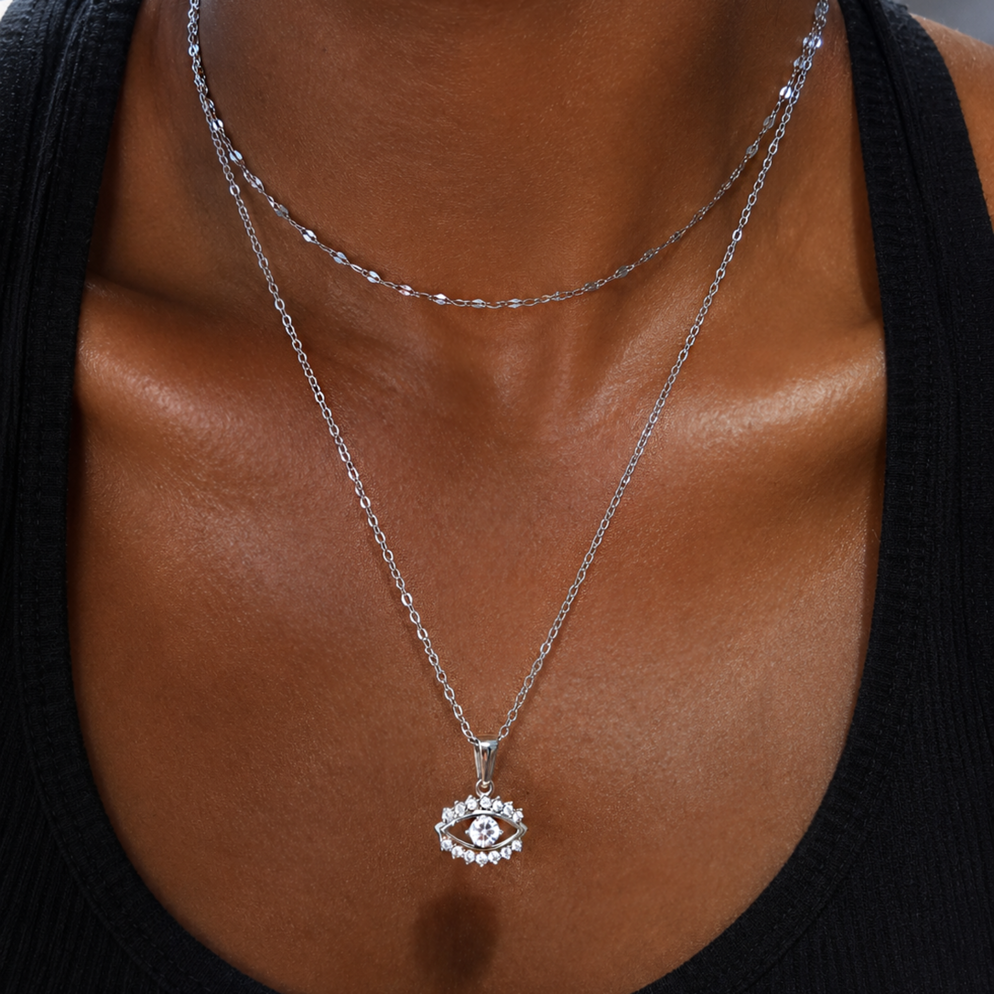 Silver lace chain necklace stacked with a silver evil eye pendant on a person wearing a black top.
