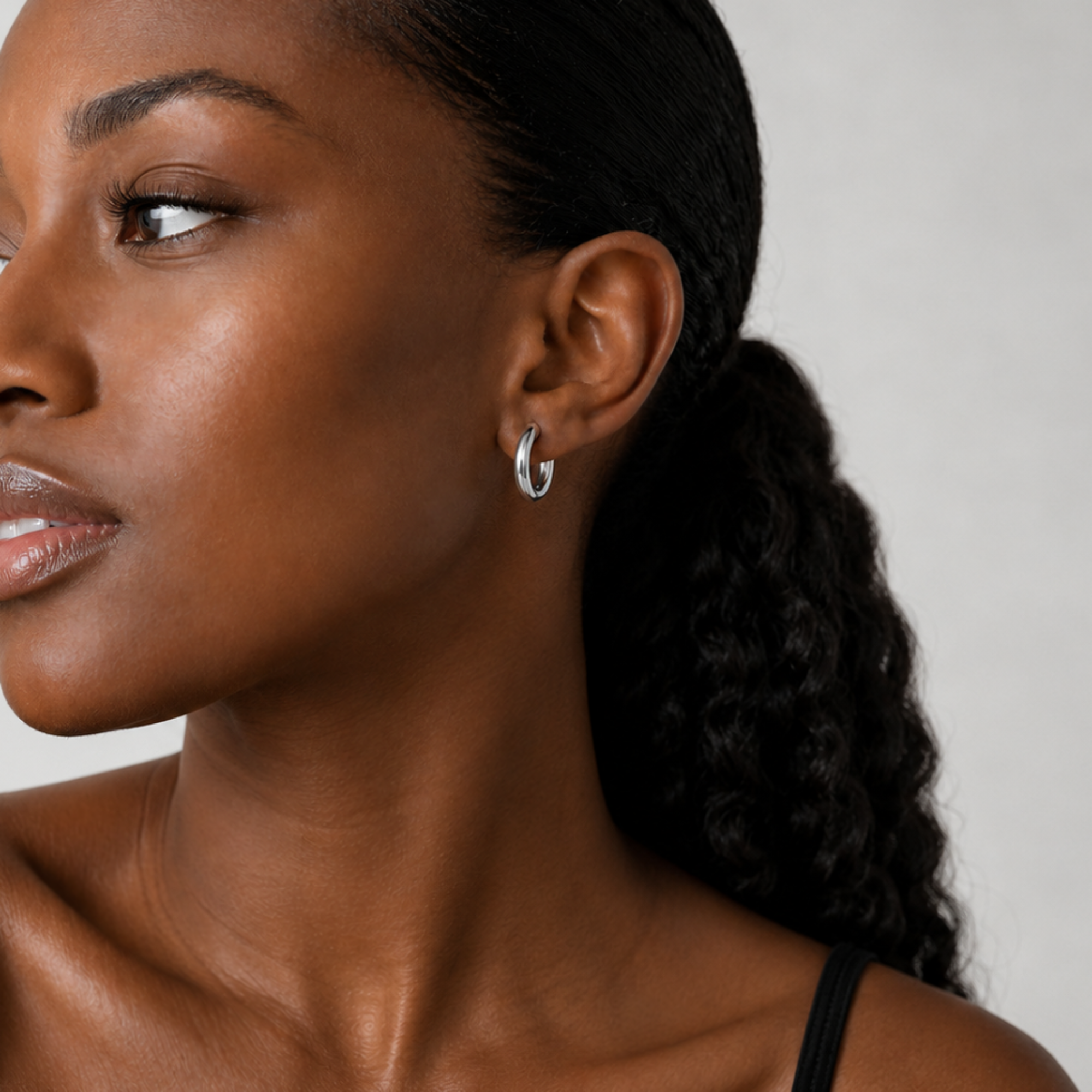 Close-up of a woman wearing a silver hoop earring against a neutral background