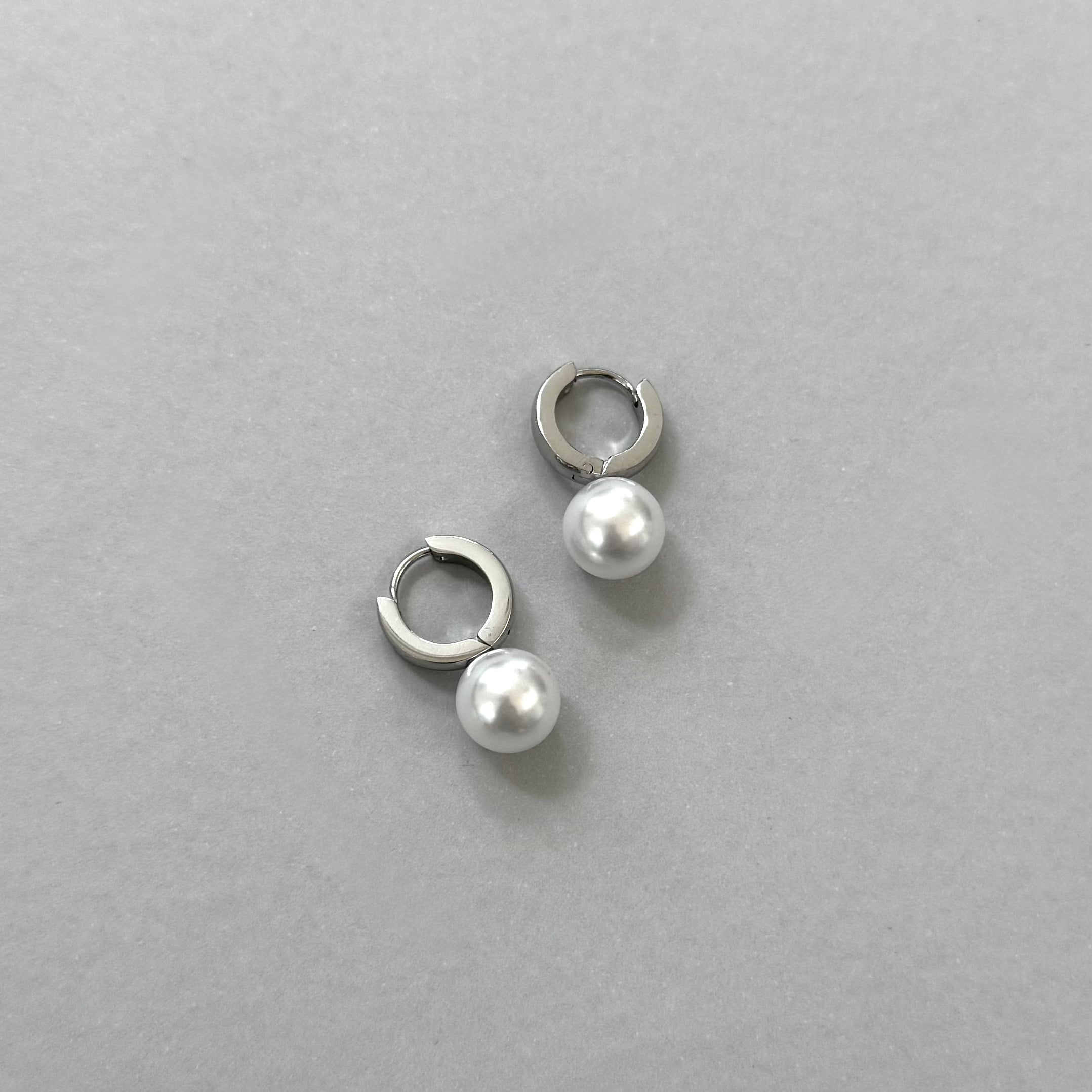 Pair of silver hoop earrings with pearl beads on a gray background