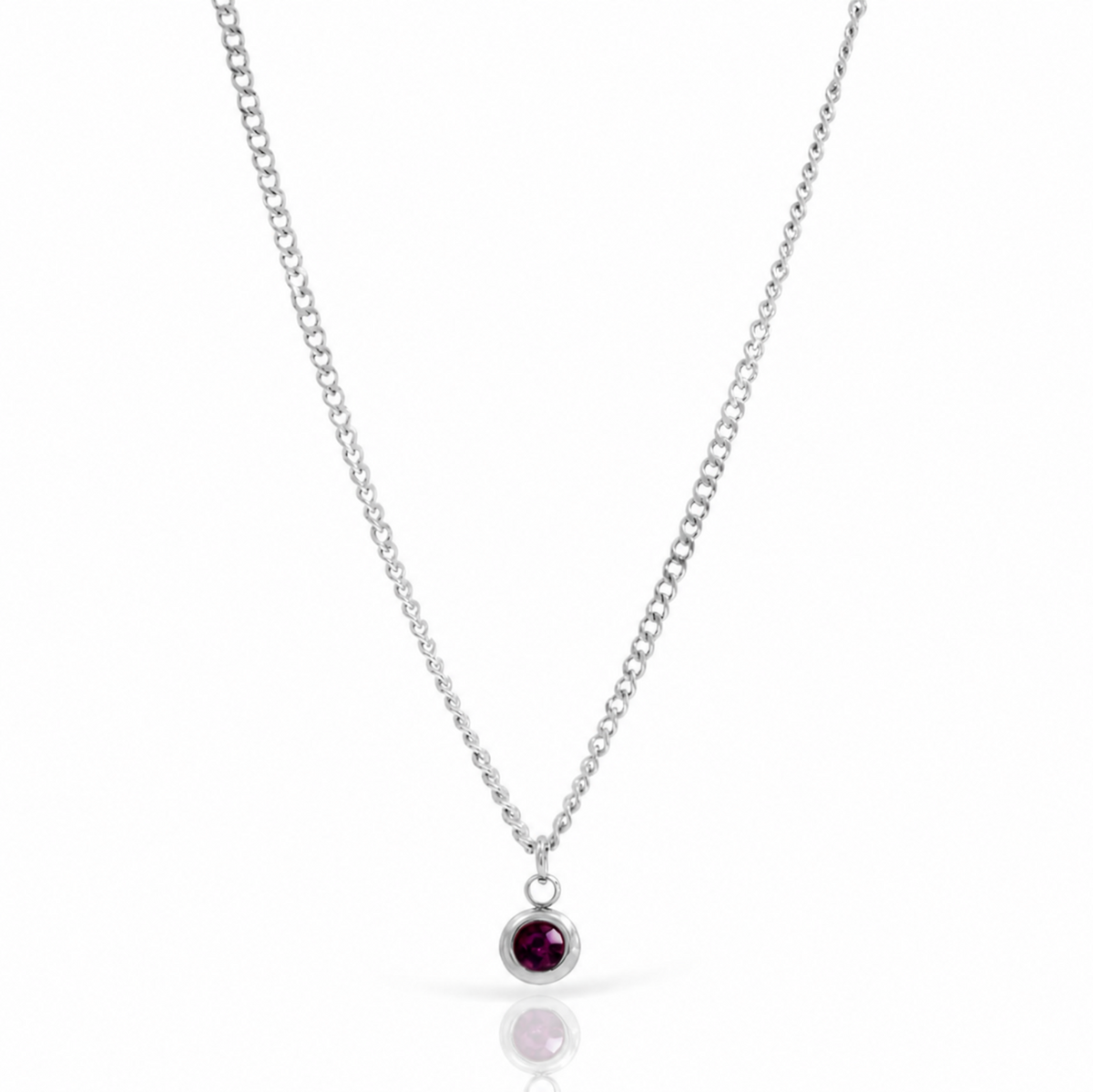 A silver chain necklace with a small round bezel-set dark red gemstone pendant, displayed on a clean white background with a soft reflection below.