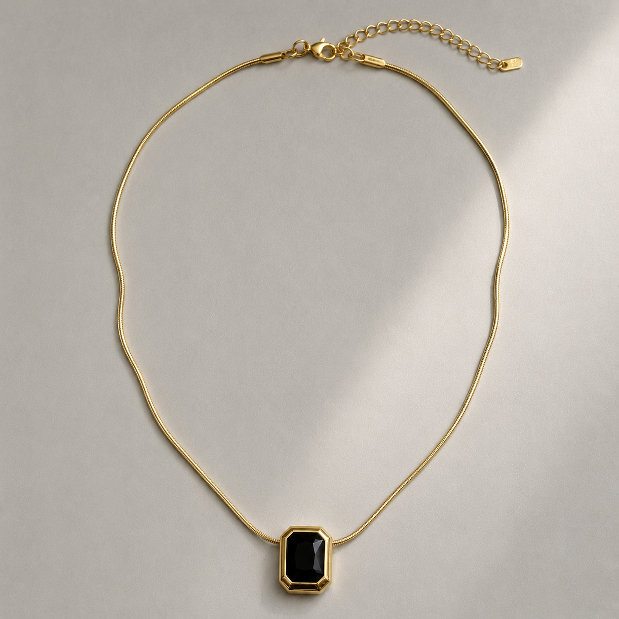 Gold necklace with a black pendant on a light gray background