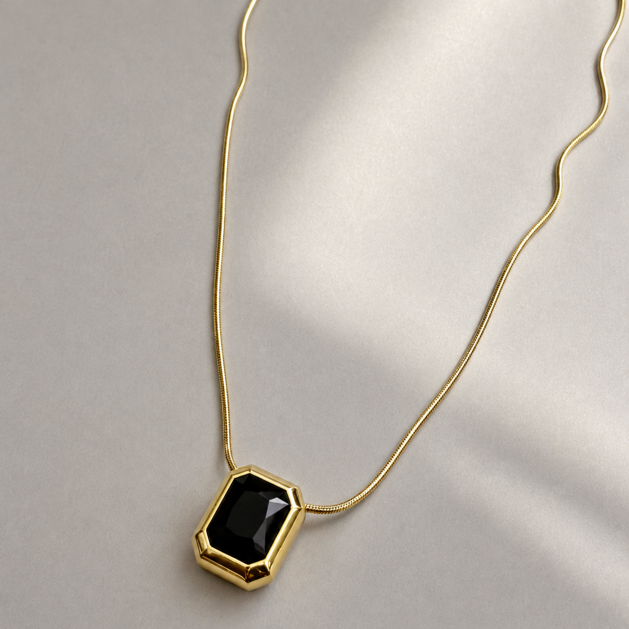 Gold necklace with a black pendant on a light gray background