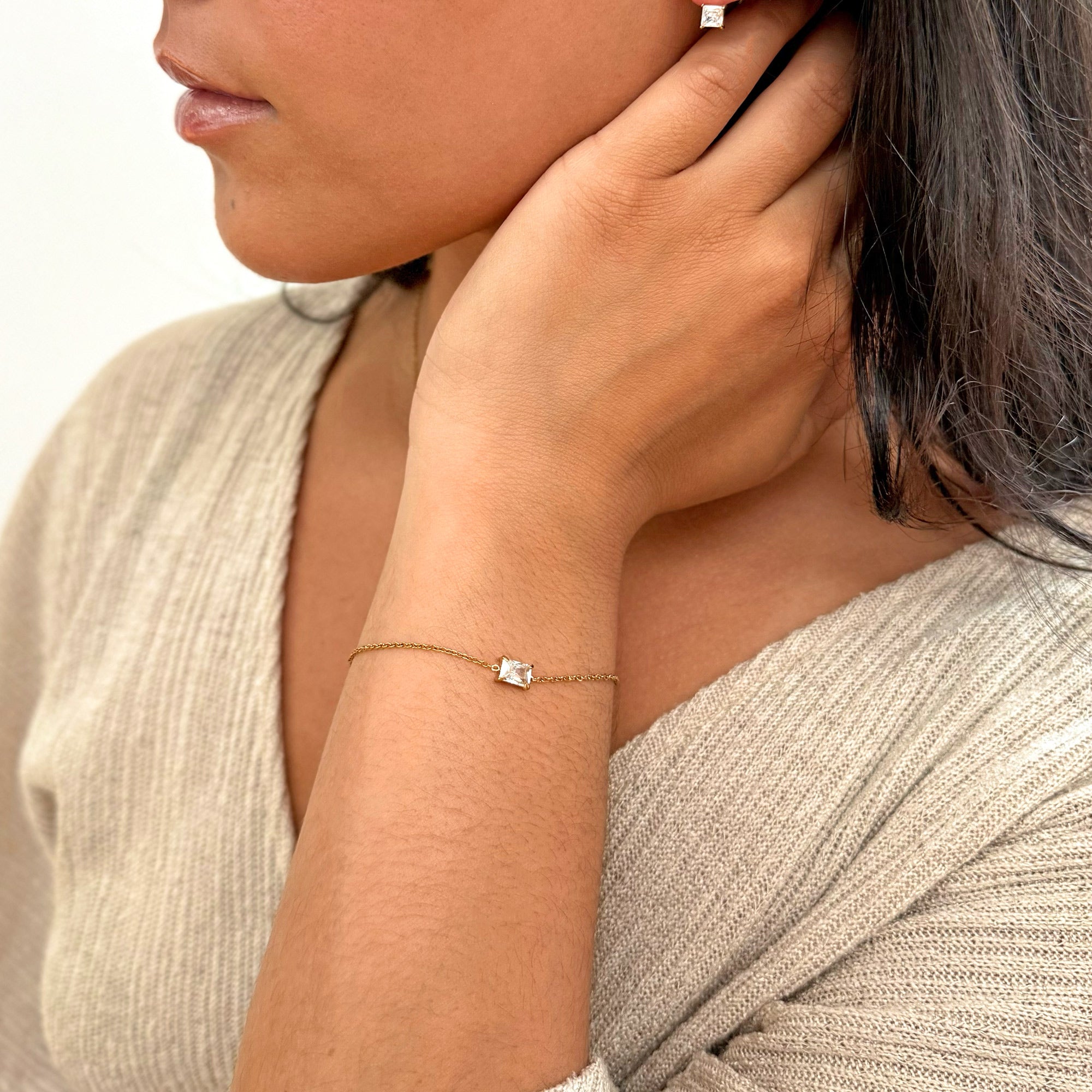 Close-up of a person wearing diamond earrings and bracelet against a neutral background