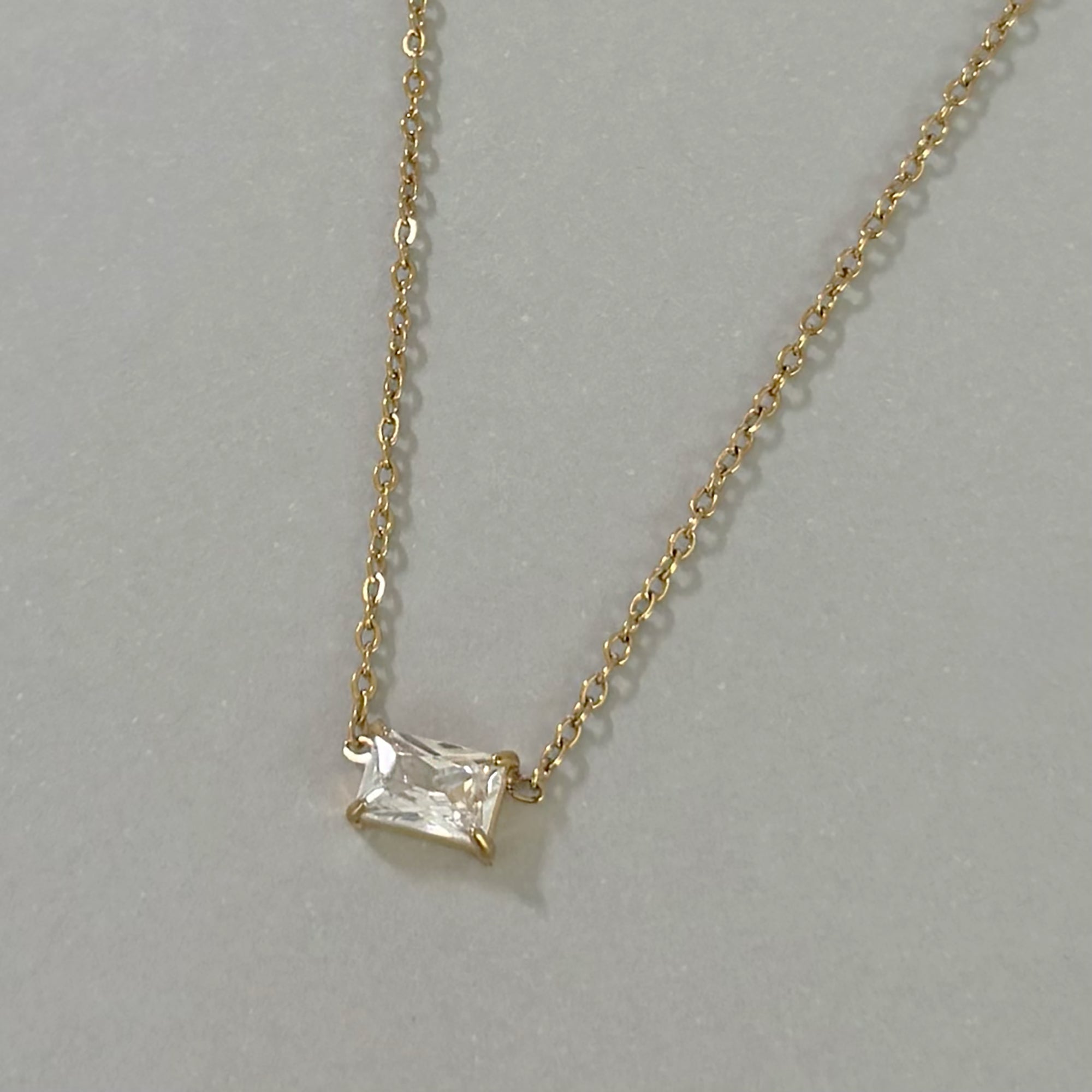 Gold necklace with a square-cut diamond pendant on a gray background