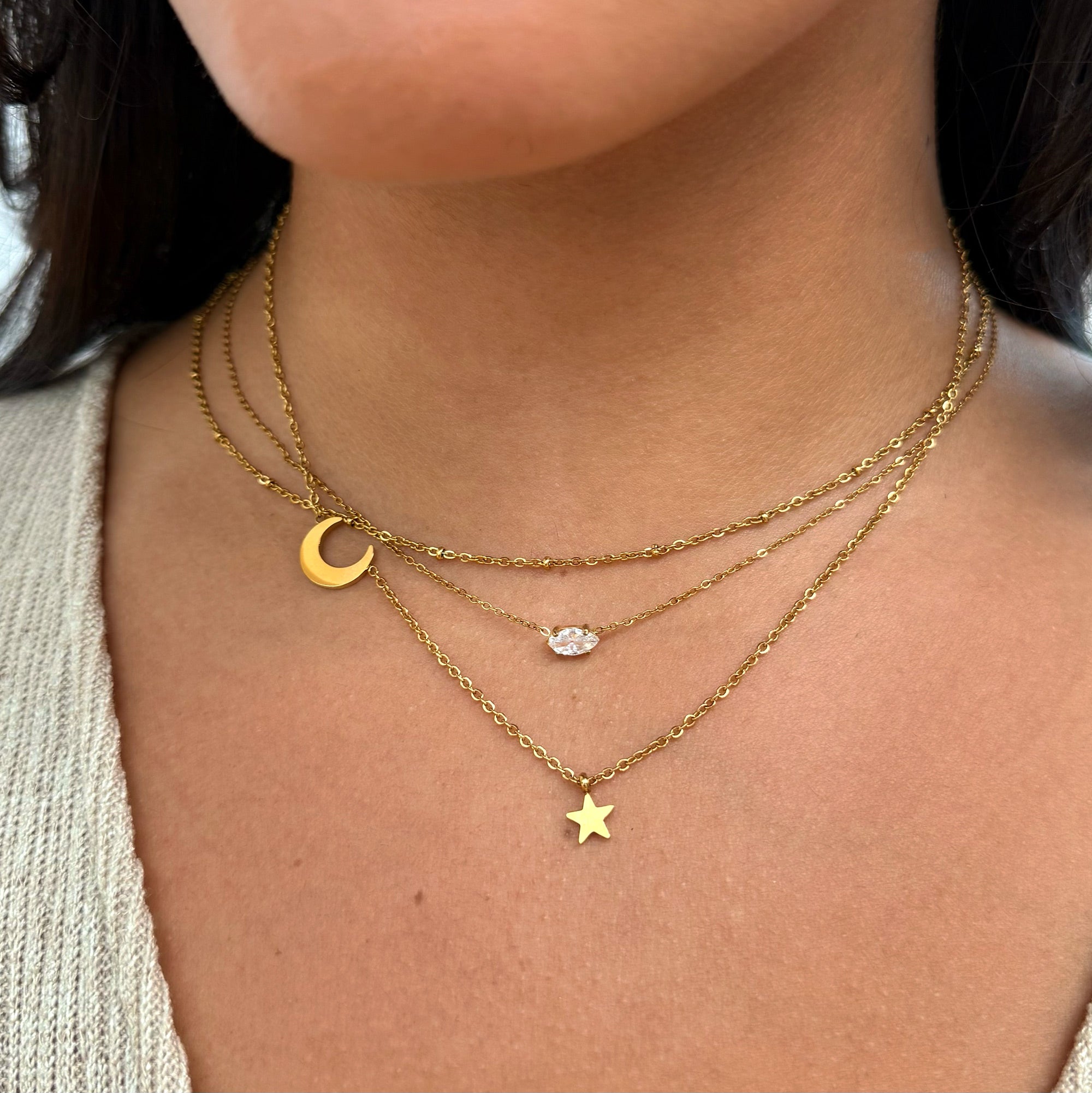 Close-up of a person wearing multiple gold necklace stack consisting of a gold dainty satellite chain with star and moon pendants and a marquis stone necklace waterproof jewelry