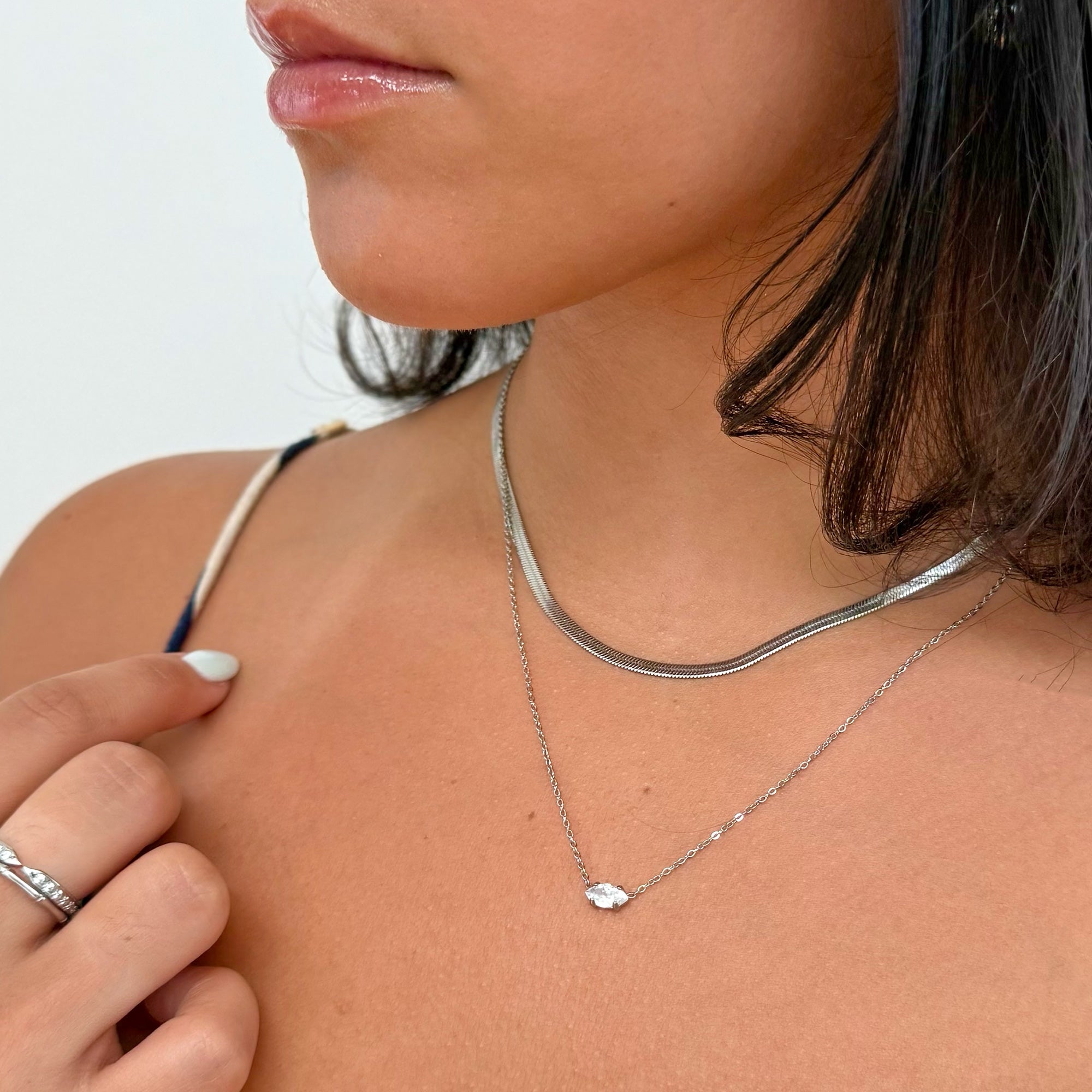 Close-up of a person wearing a silver snake chain necklace with a dainty silver marquis pendant necklace waterproof jewelry