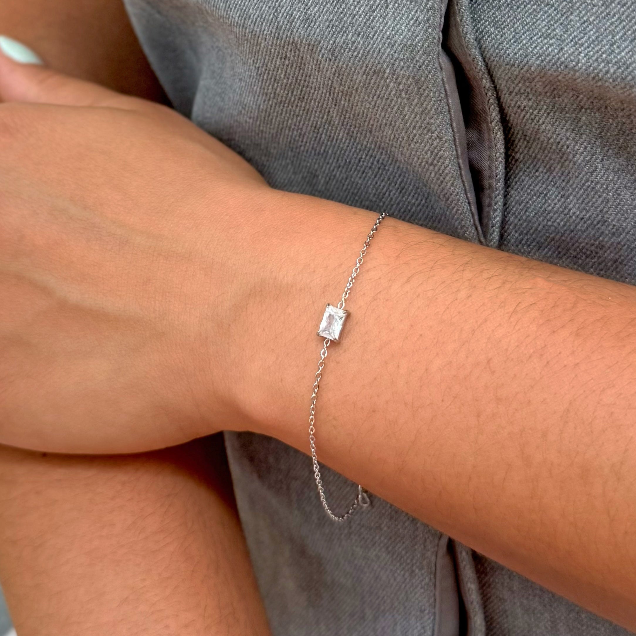Silver bracelet with a square pendant on a wrist against a gray background