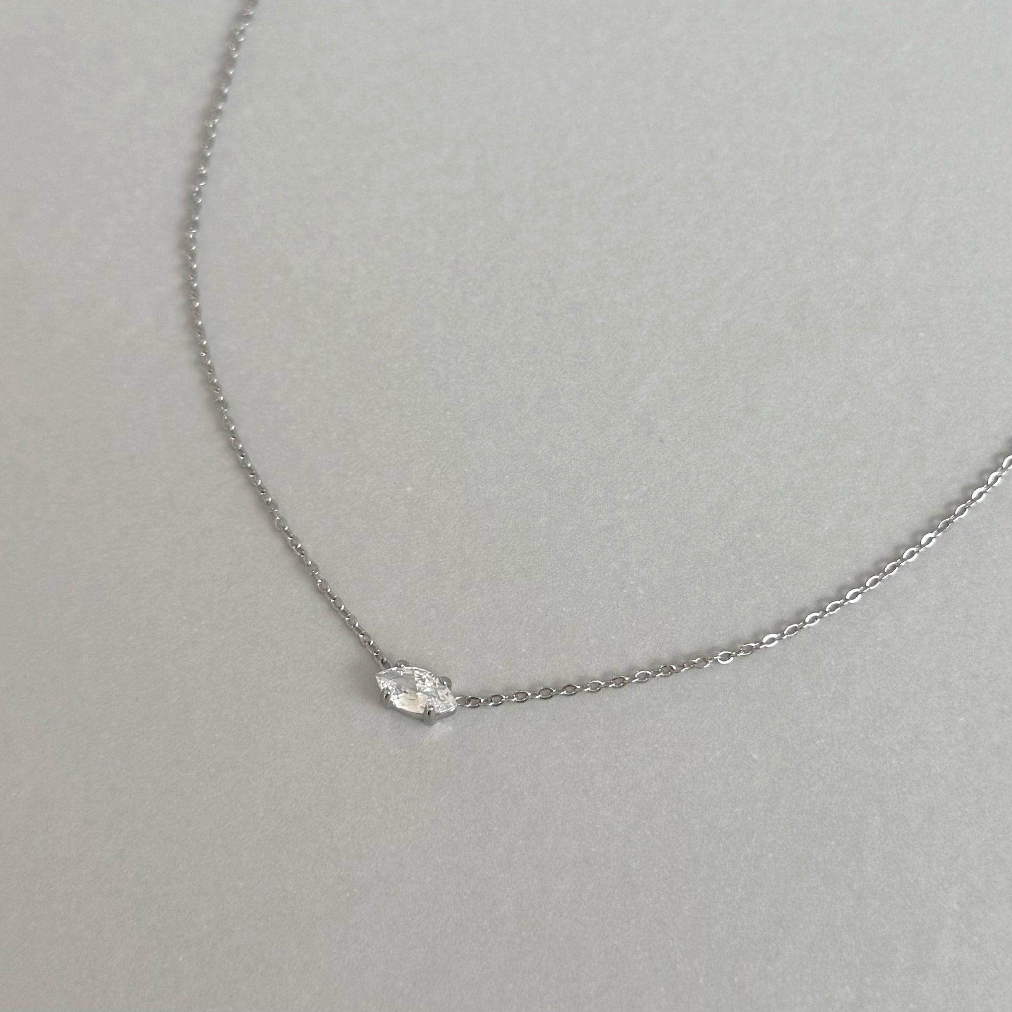 Silver necklace with a small diamond marquis pendant on a light gray background waterproof jewelry
