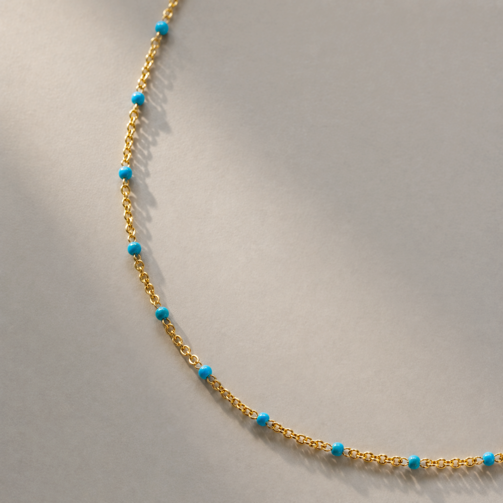 Gold chain necklace with blue turquoise beads on a neutral background