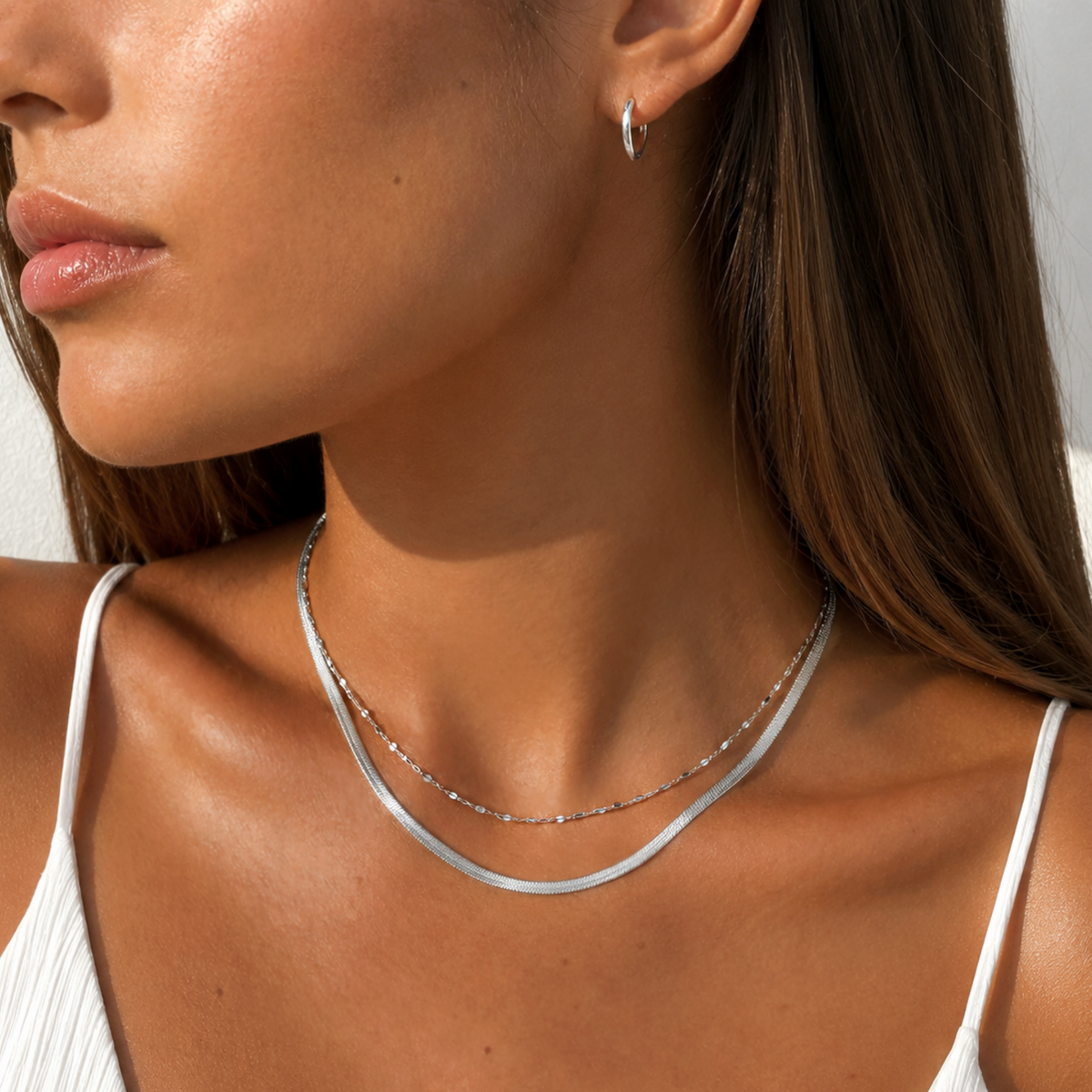 A close-up lifestyle shot of a woman wearing a double-layered silver necklace, featuring a silver dainty lace chain and a delicate lacechain, paired with a small silver hoop earring.