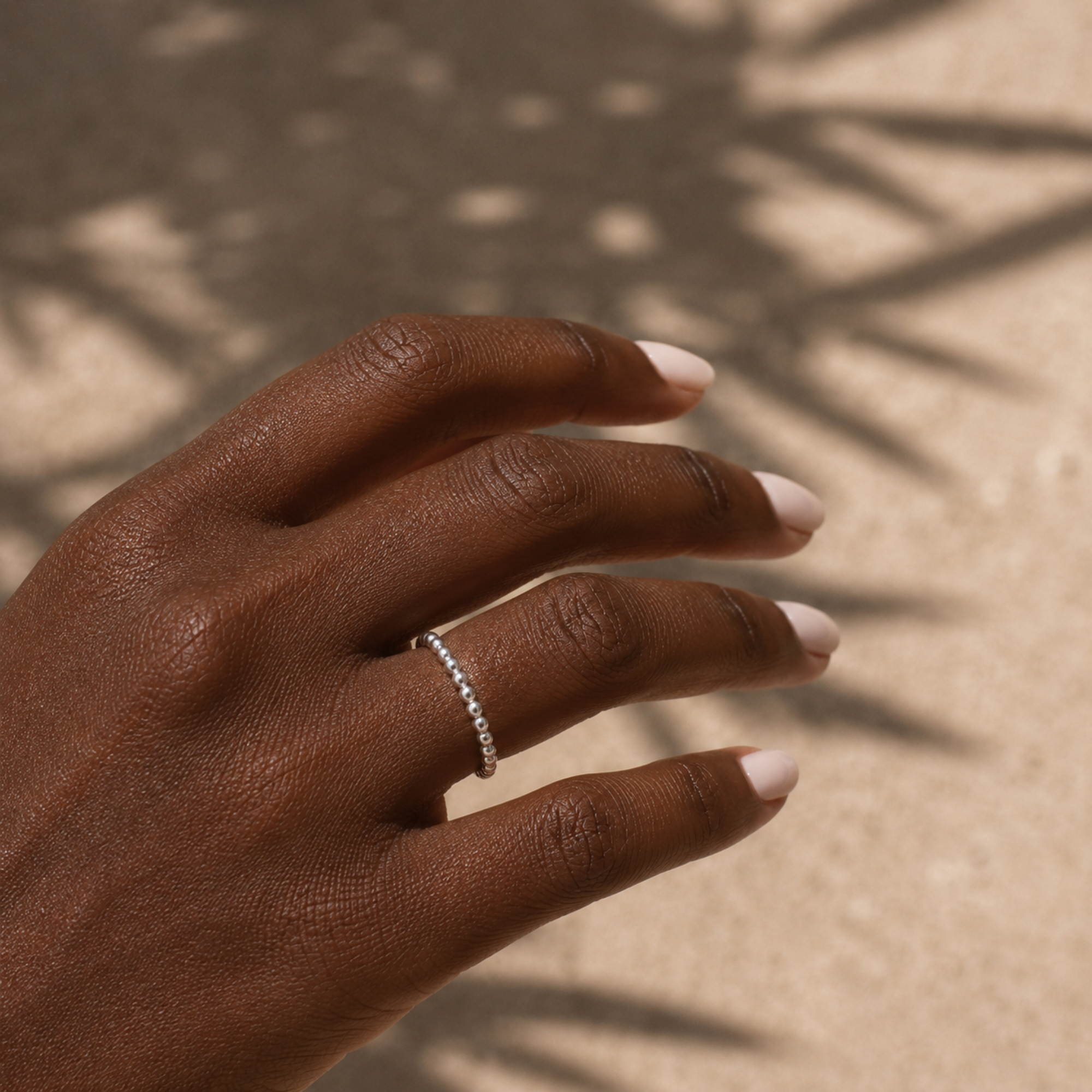 Hand wearing a dainty silver beaded ring with a neutral background