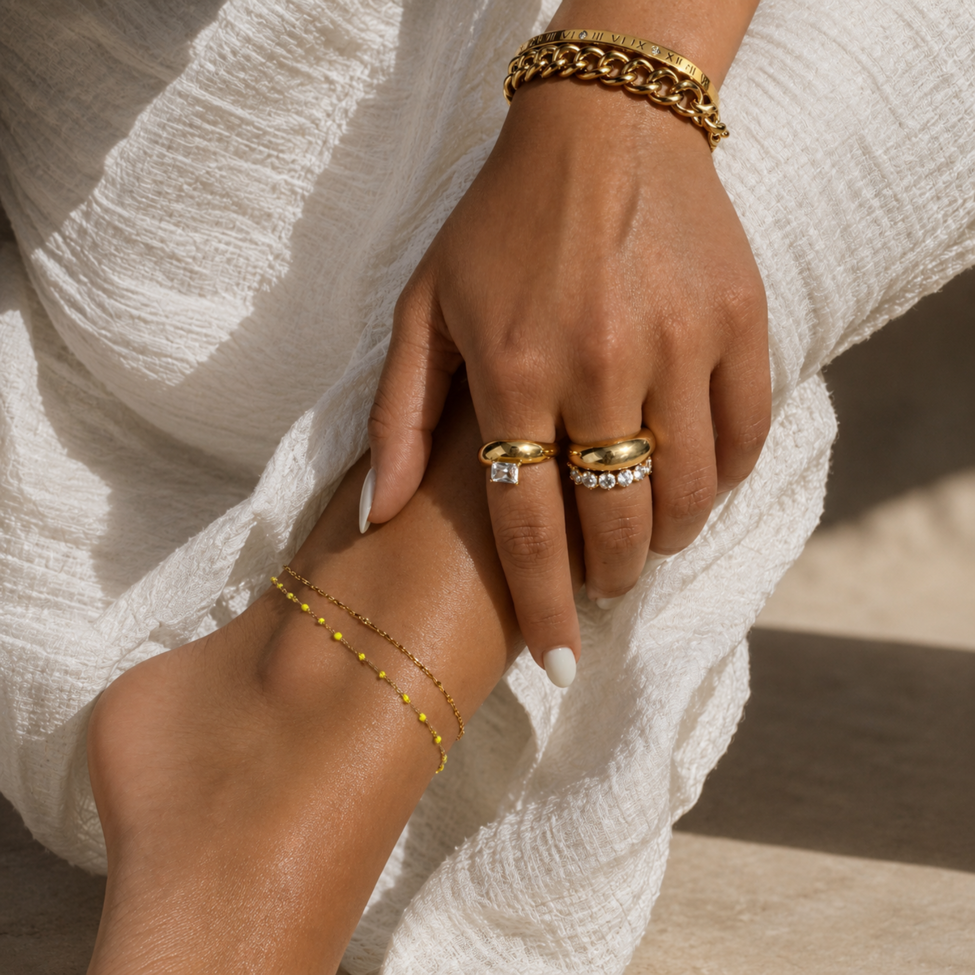 Close-up of a hand and foot wearing gold jewelry against a neutral background