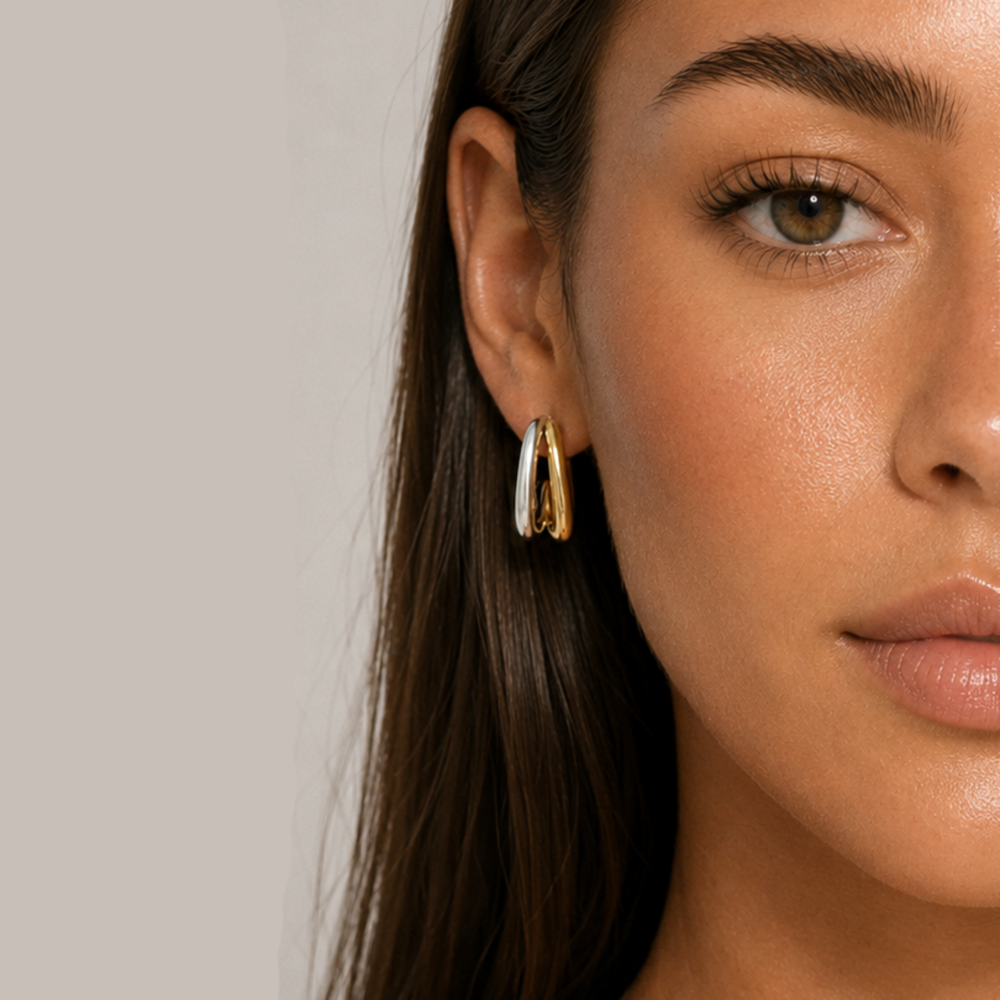 Close-up of a woman wearing dual tone double oval hoop earrings against a neutral background