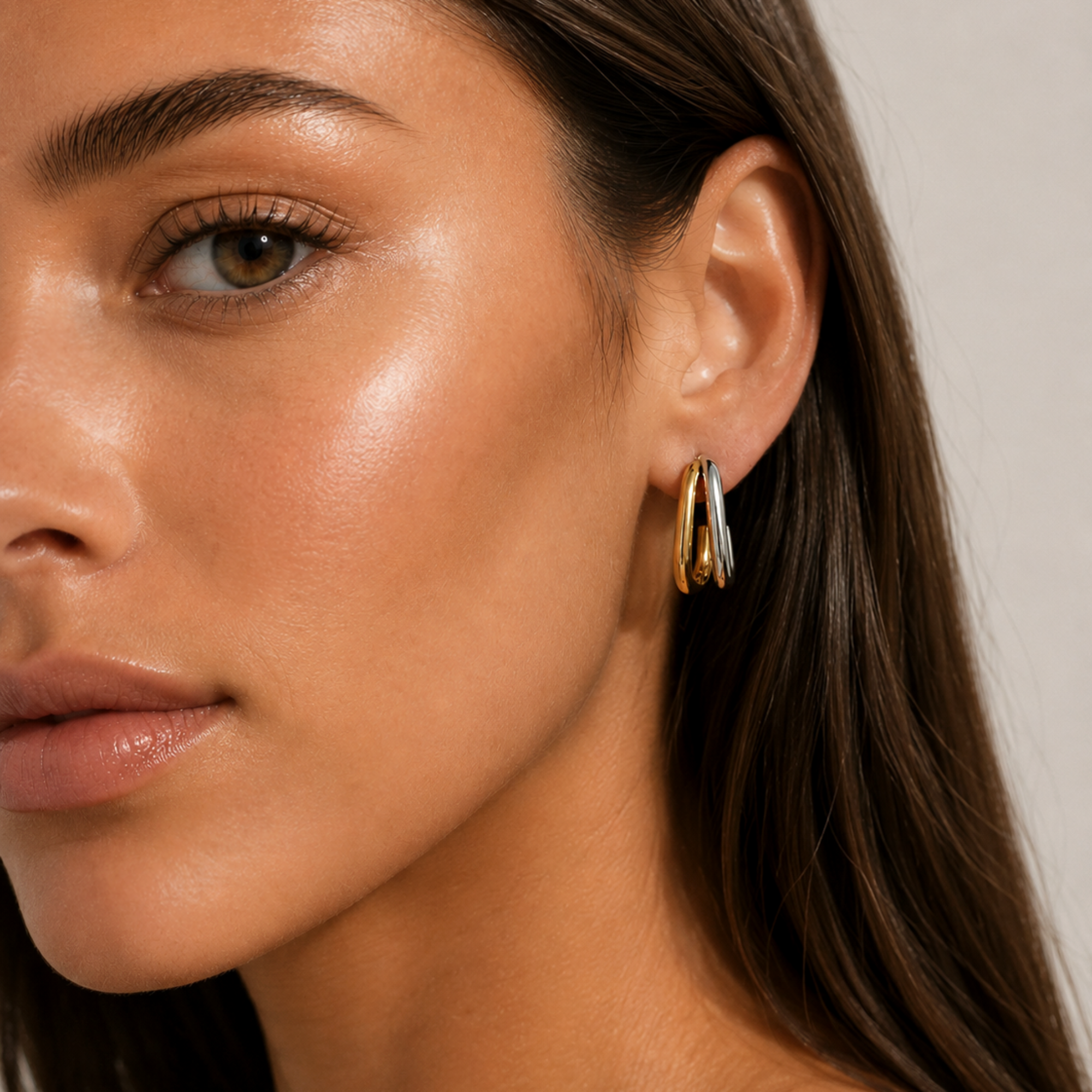 Close-up of a woman wearing dual tone double hoop earrings with a neutral background