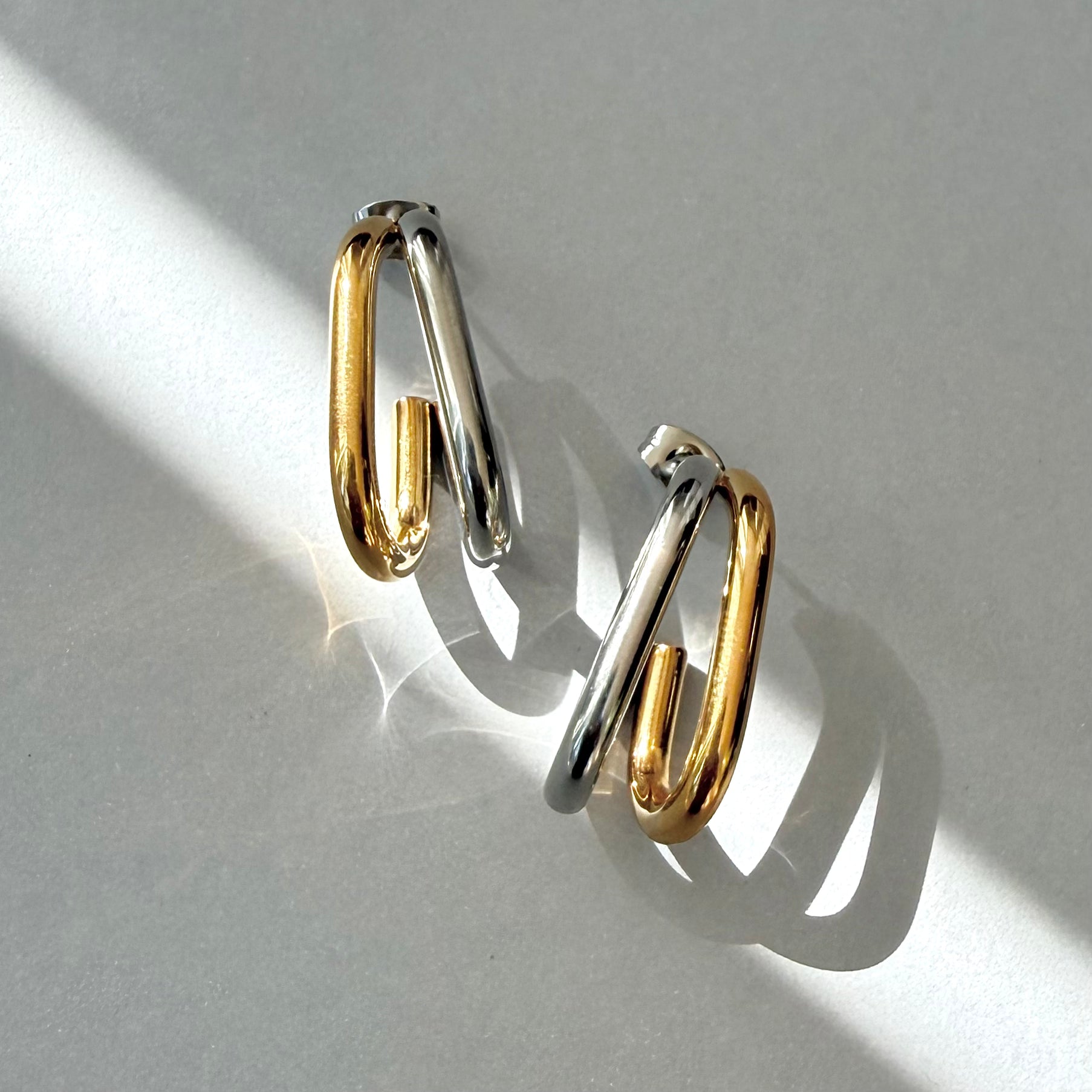 Pair of dual tone double U hoop earrings on a light gray background