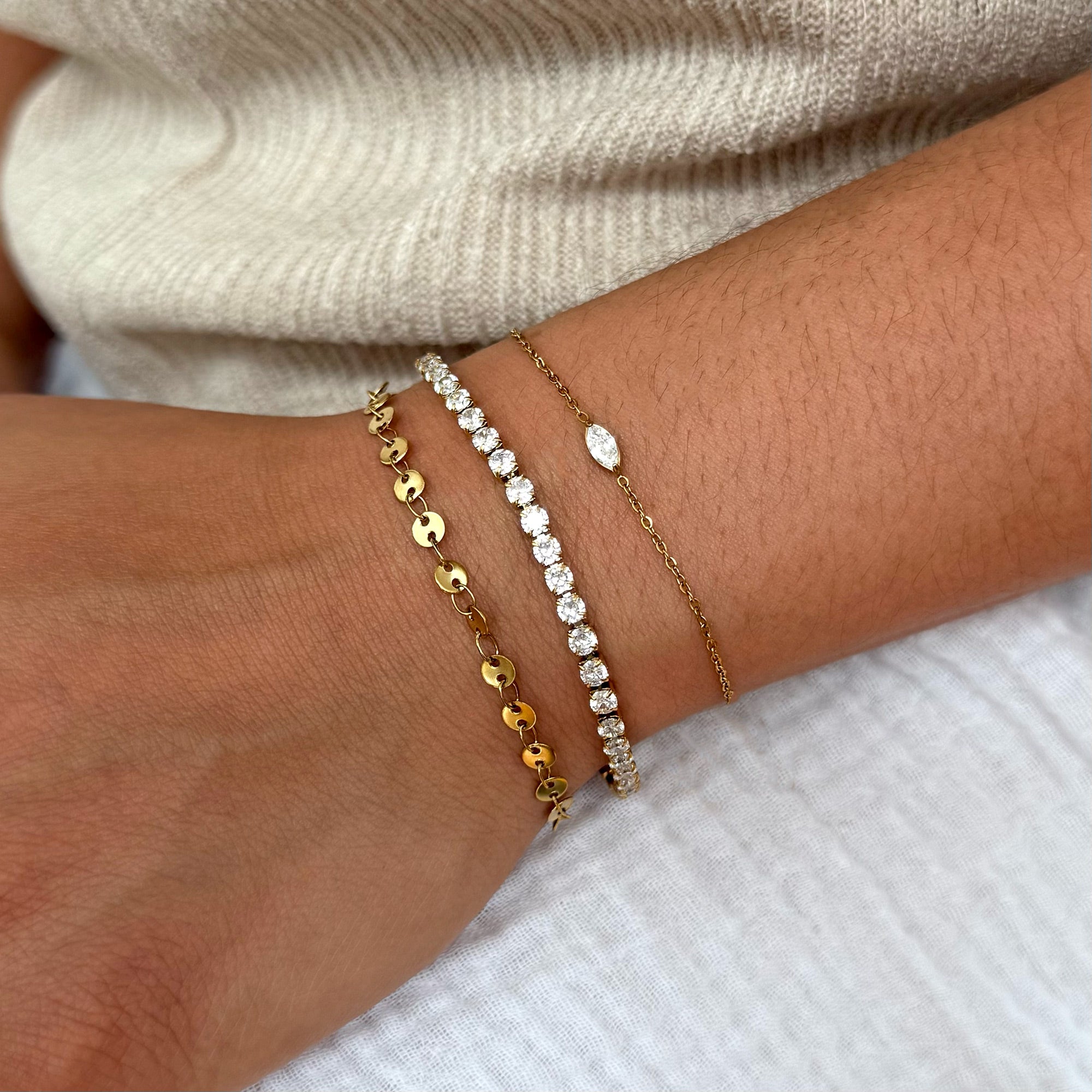 Three gold and silver bracelets on a wrist against a neutral background highlighting the marquis bracelet