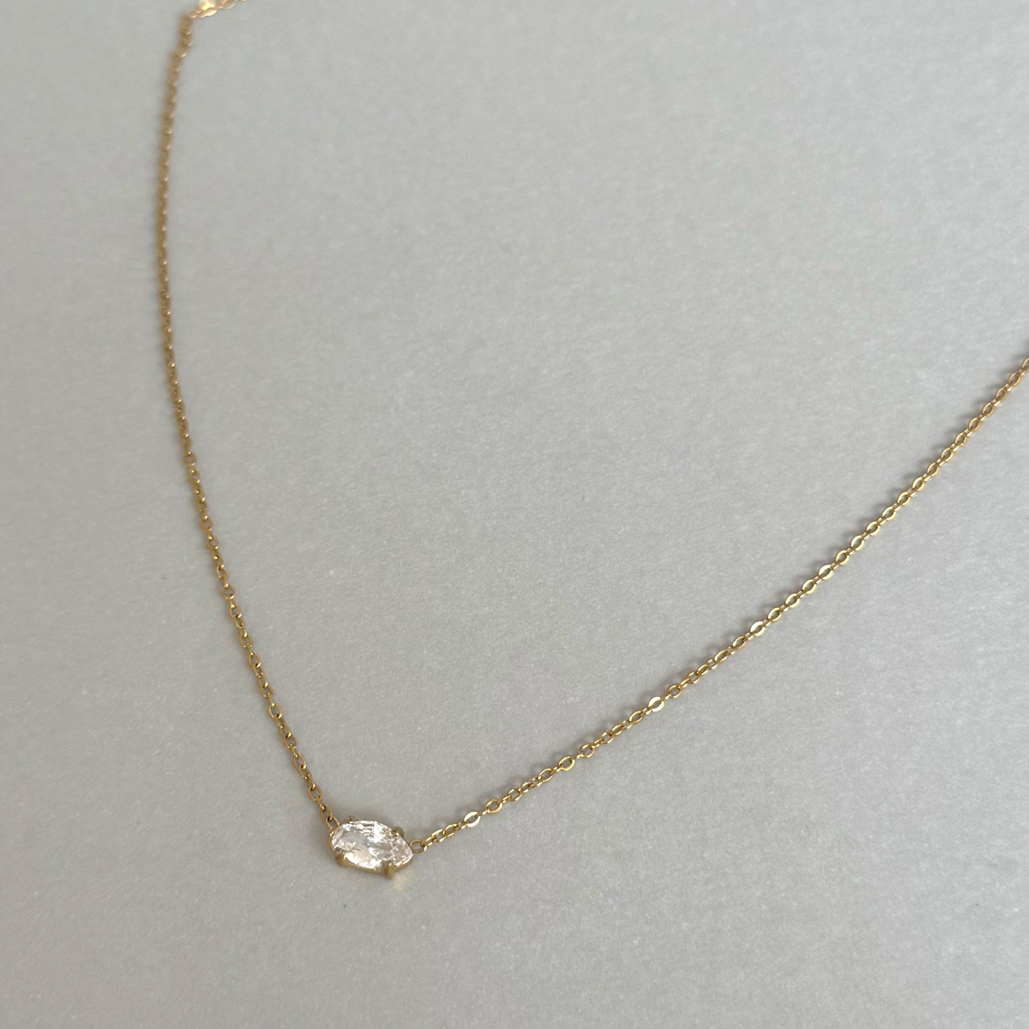 Gold necklace with a small marquis diamond pendant on a light gray background tarnish free jewelry