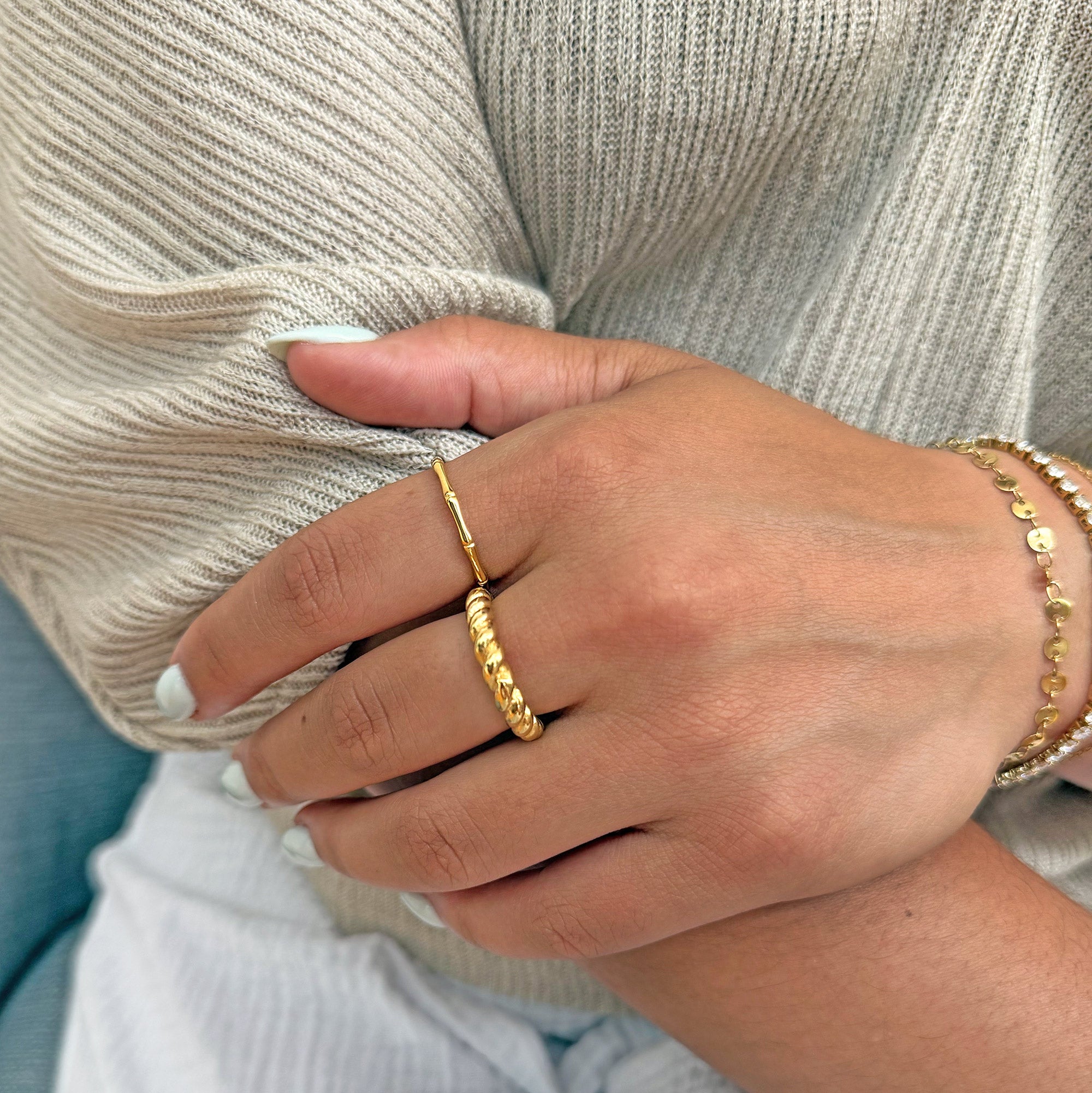 Hand wearing a gold ring stack consisting of thin gold bamboo ring and a gold twist ring against a neutral background tarnish free jewelry