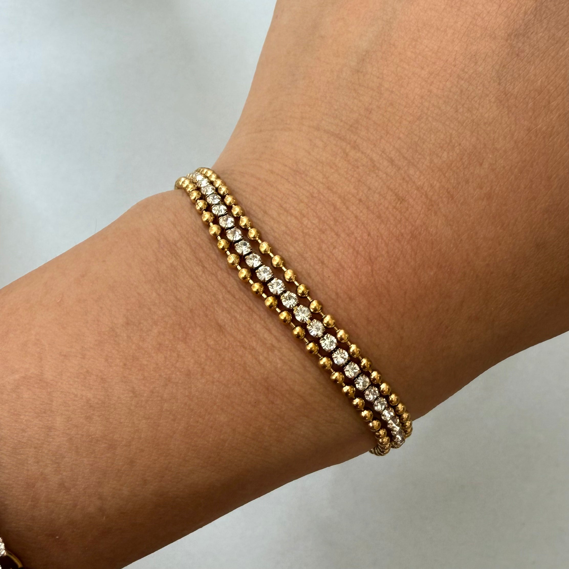 Gold bracelet stacked with beaded chain on a wrist against a neutral background
