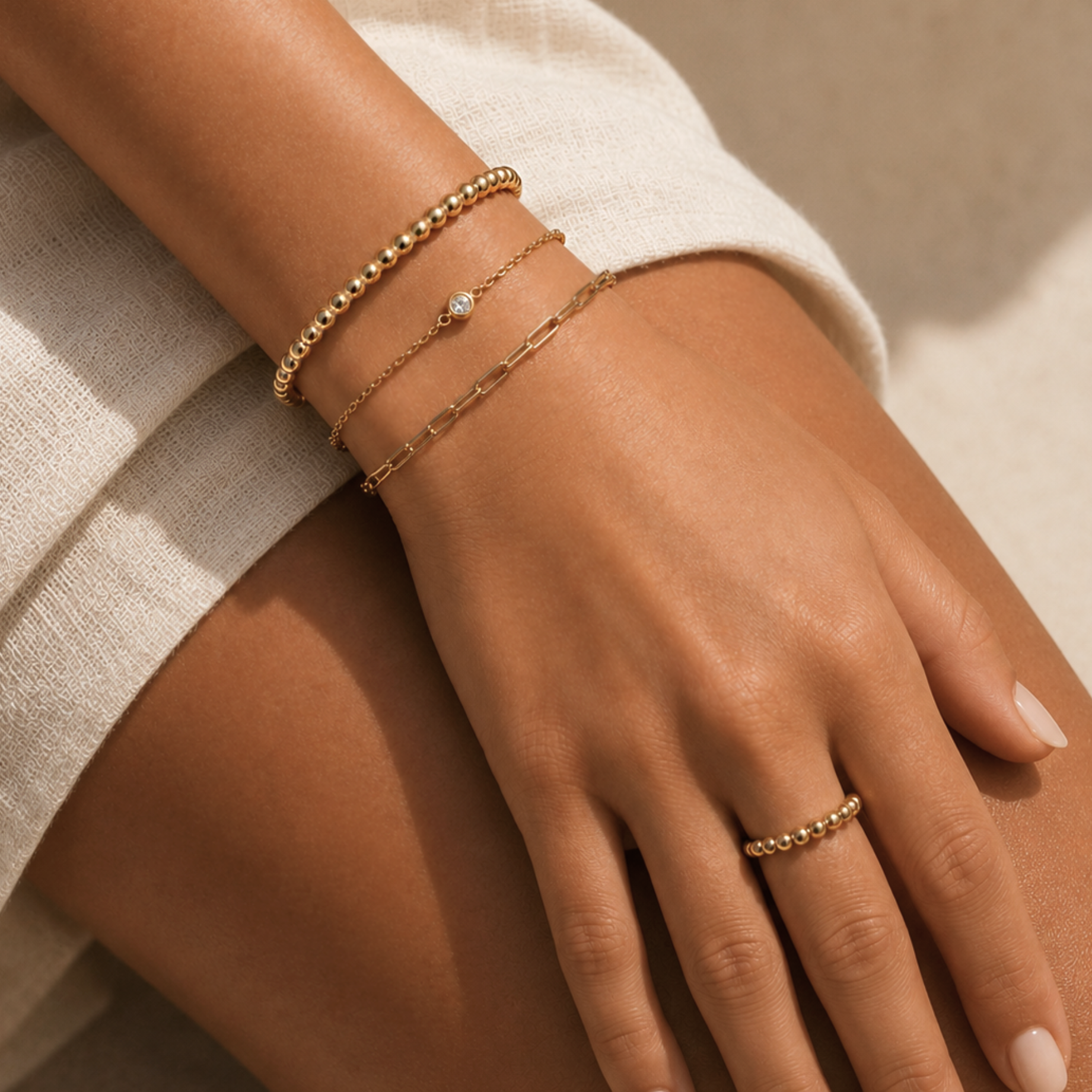 Close-up of a hand wearing gold bracelets and a ring on a neutral background