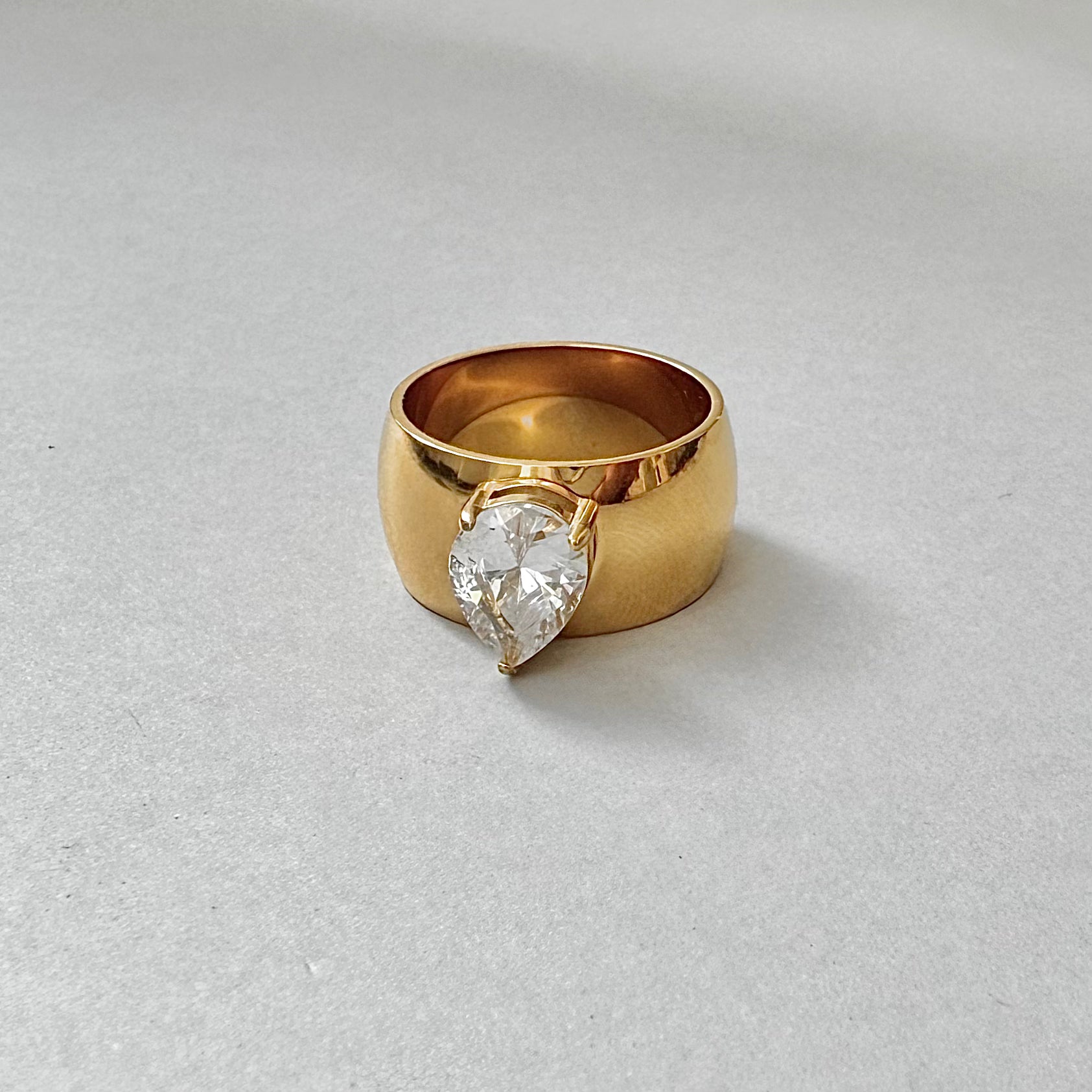 Gold ring with a pear-shaped diamond on a light gray background