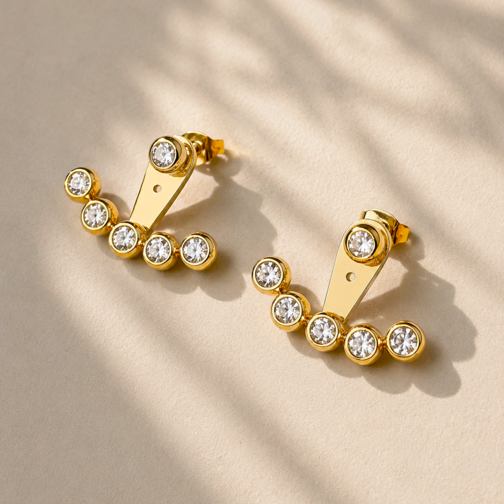 Gold ear jacket earrings with clear gemstones on a beige background