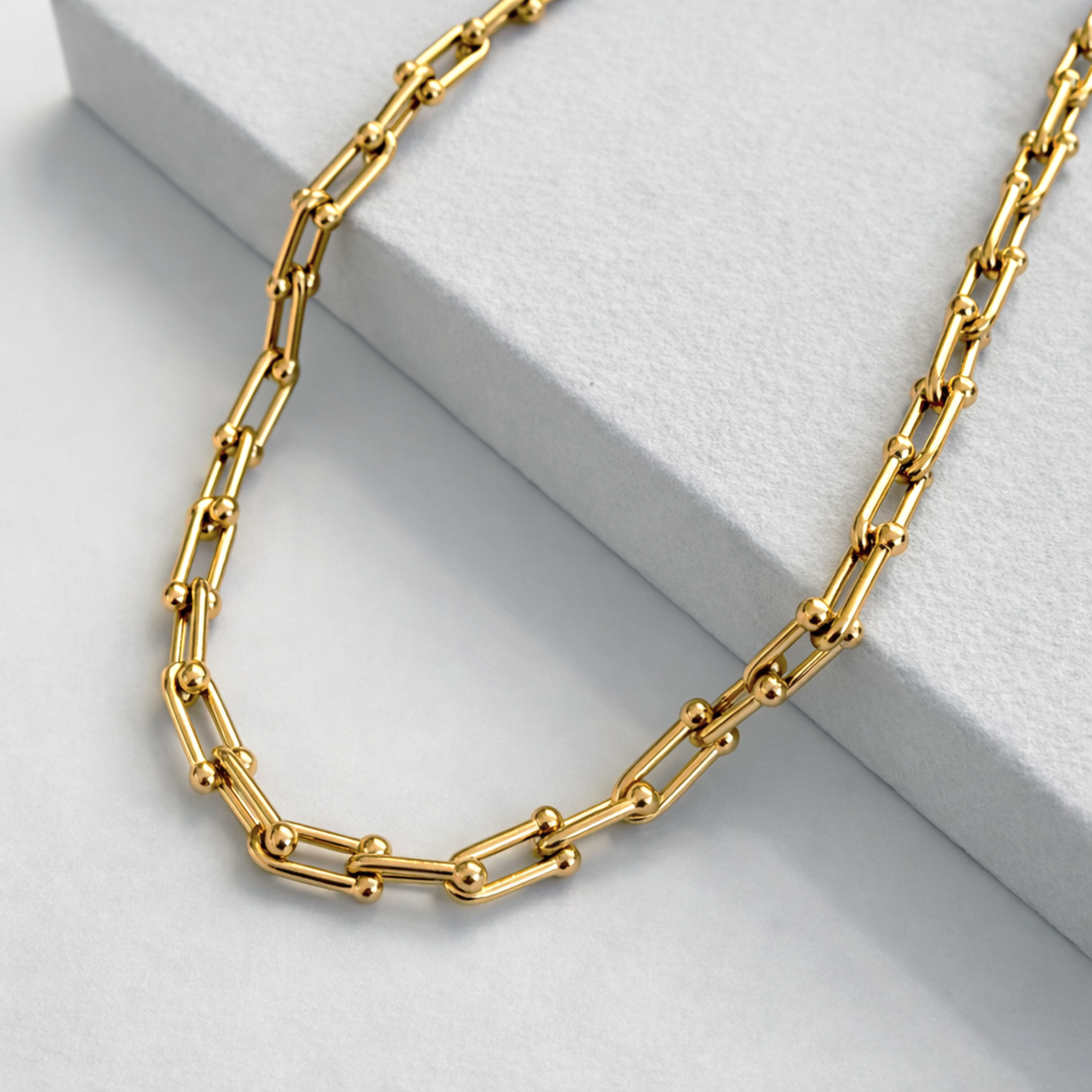 Gold hardware chain necklace on a light gray surface