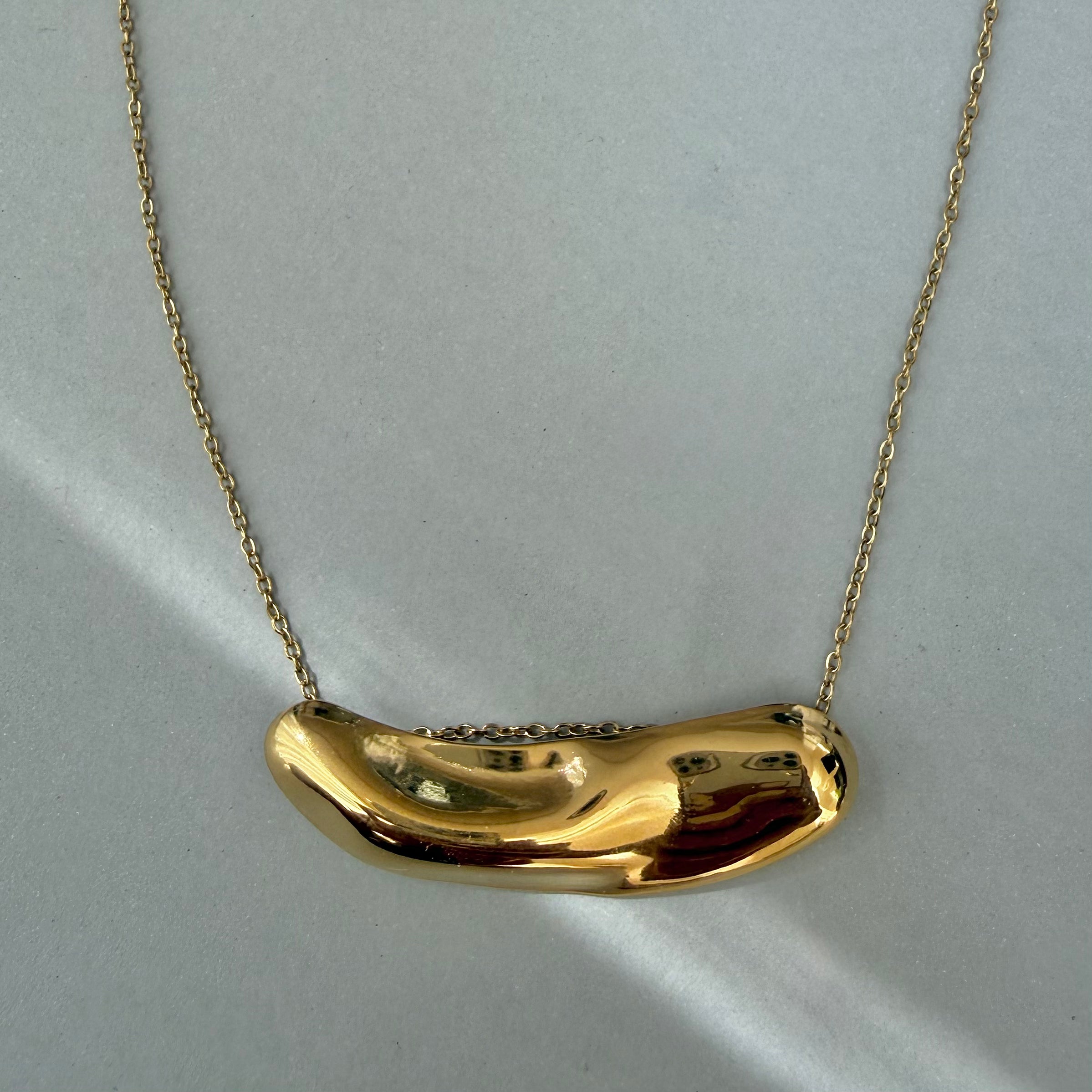 Gold necklace with a unique pendant on a light gray background