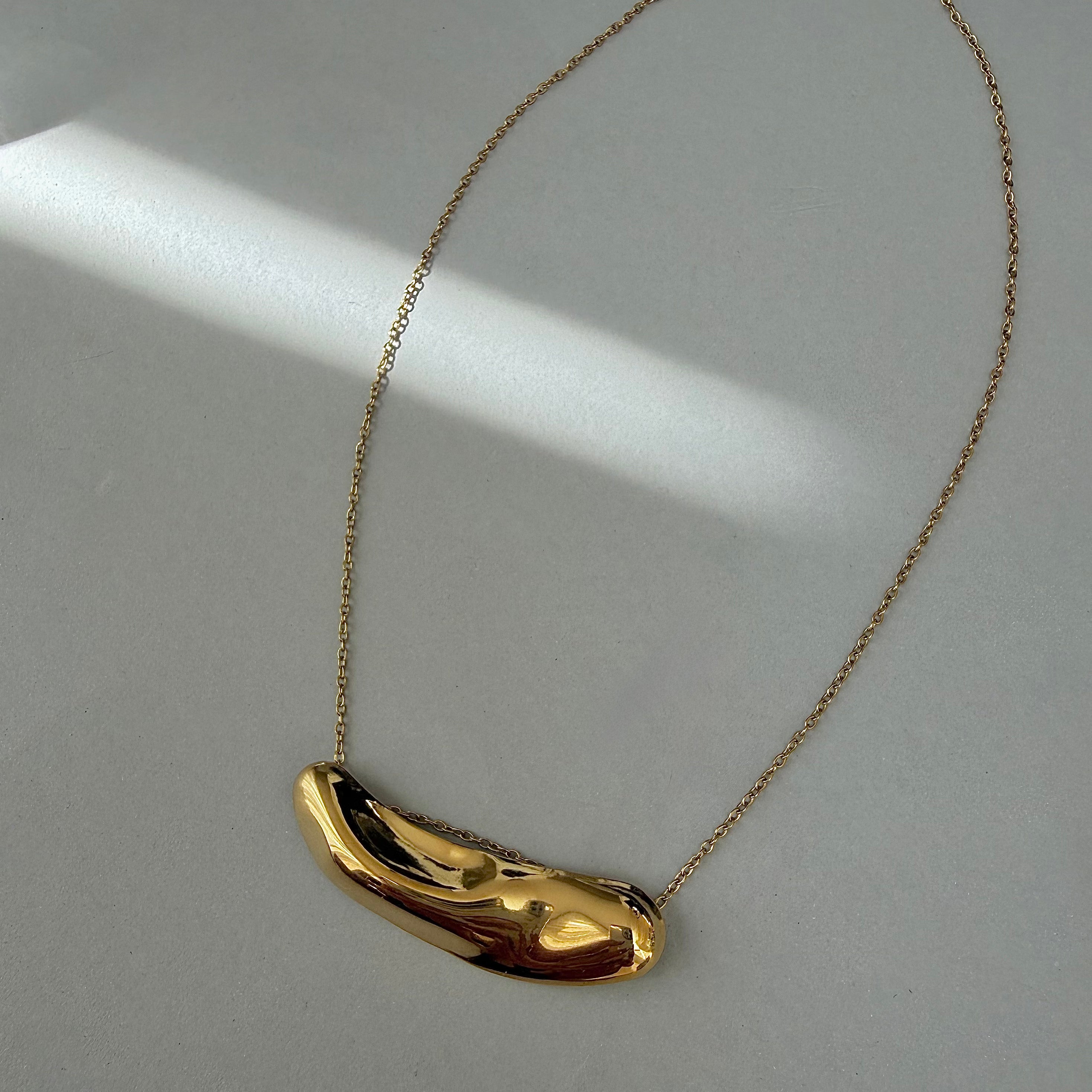 Gold molten bar pendant on a chain against a light gray background