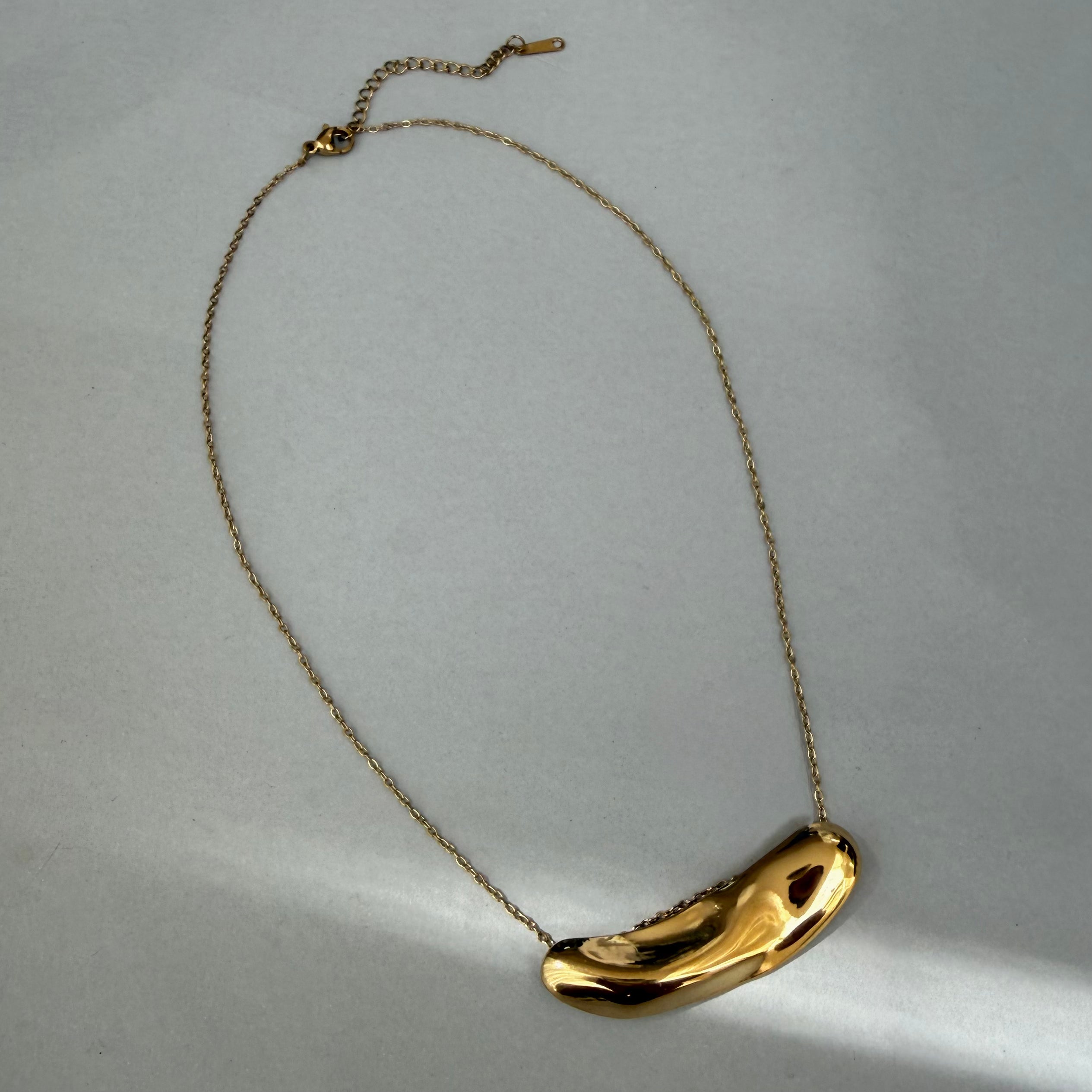Gold necklace with a unique molten bar staement pendant on a light gray background