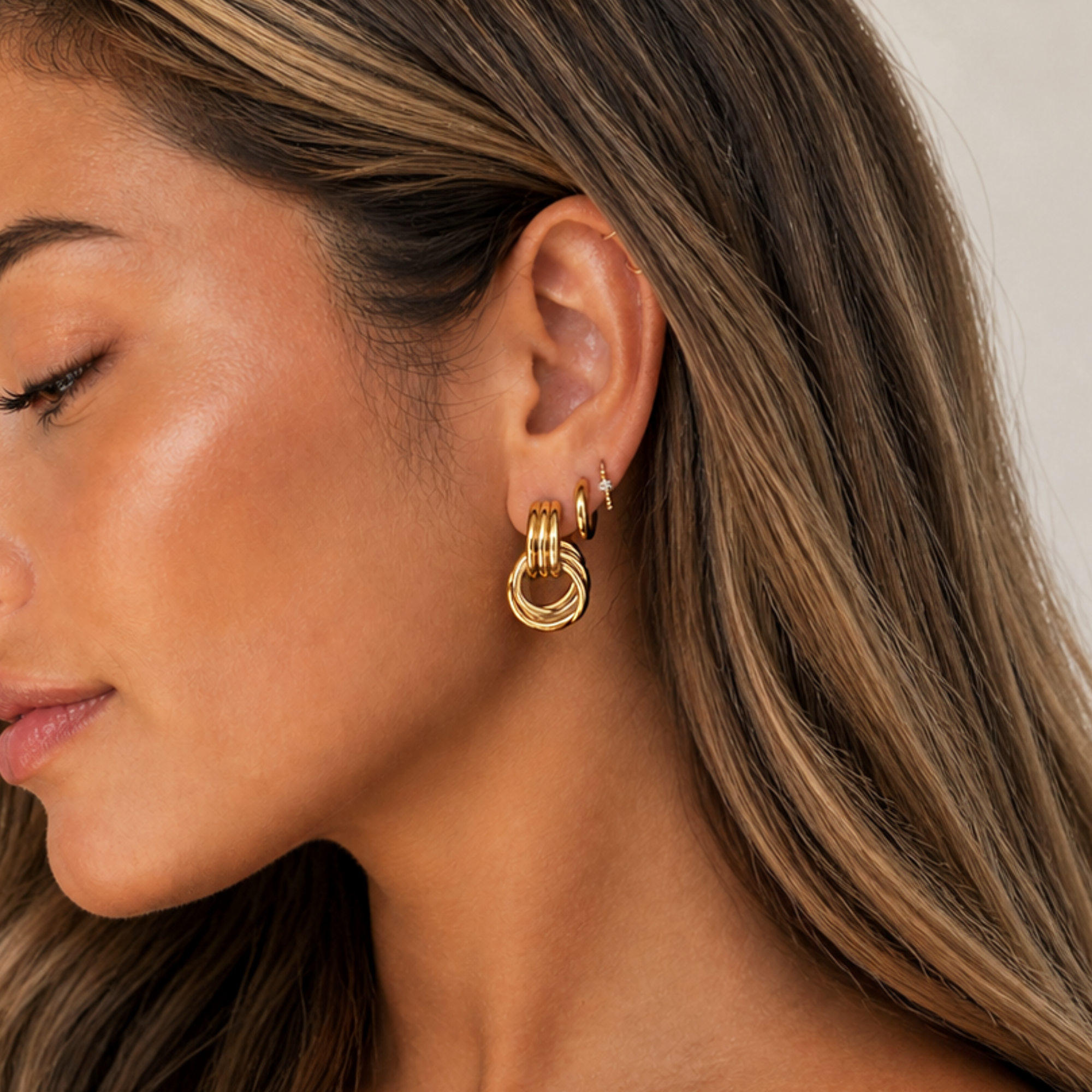 Close-up of a woman wearing gold door knocker earrings with a neutral background