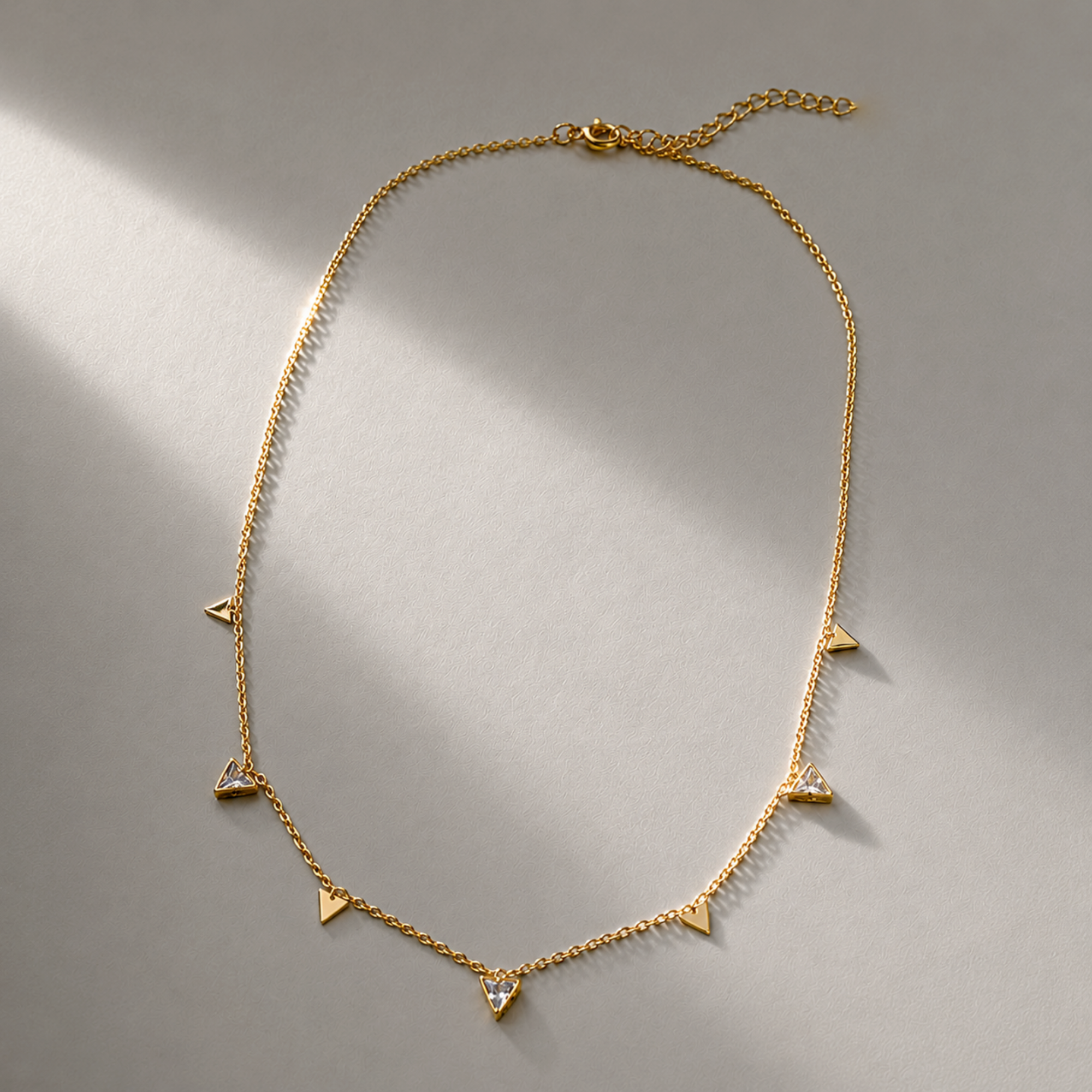 Gold necklace with heart and triangle pendants on a gray background