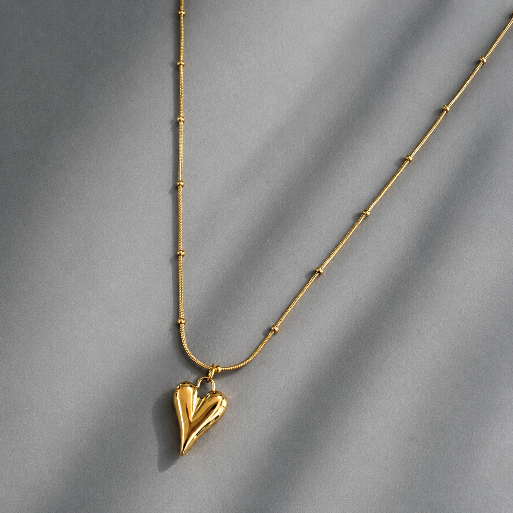 Gold necklace with a heart-shaped pendant on a gray background