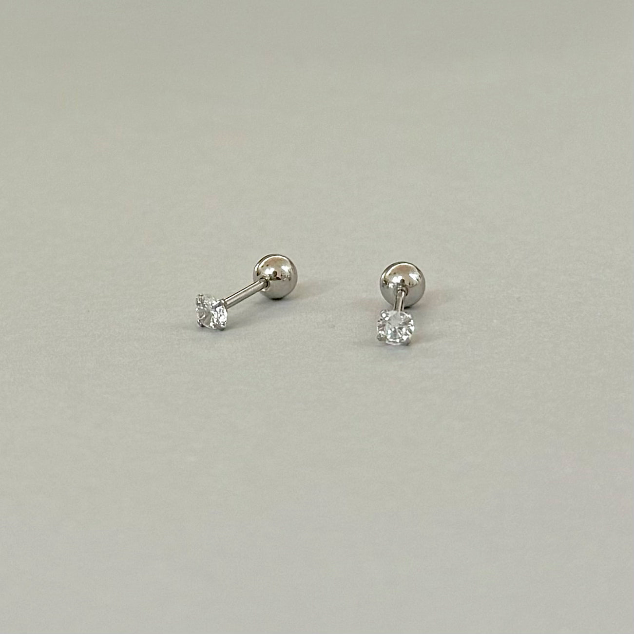 Pair of silver diamond stud earrings with screw back closure comfort fit on a light gray background waterproof jewelry