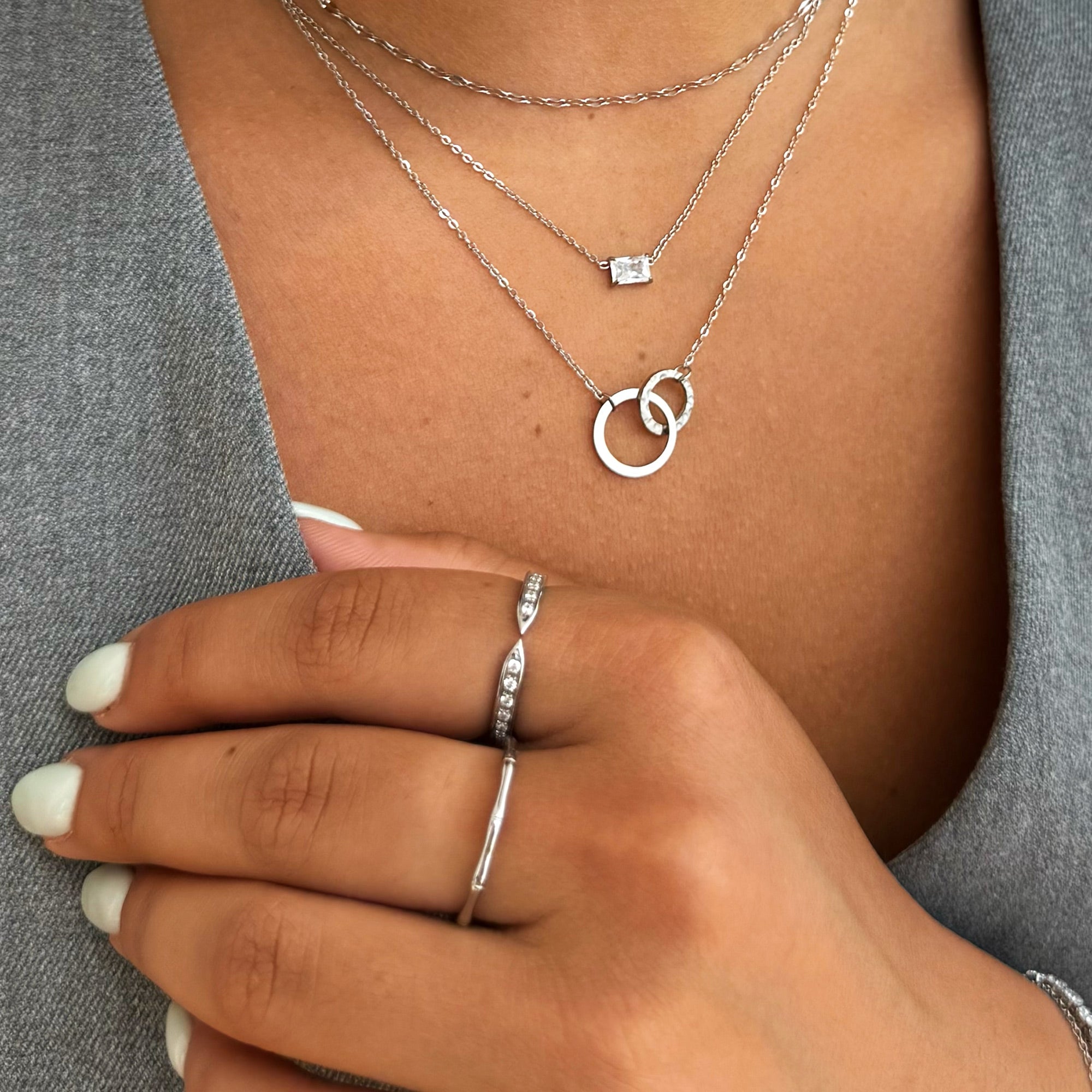 Silver necklaces and rings on a person's hand and chest against a gray background