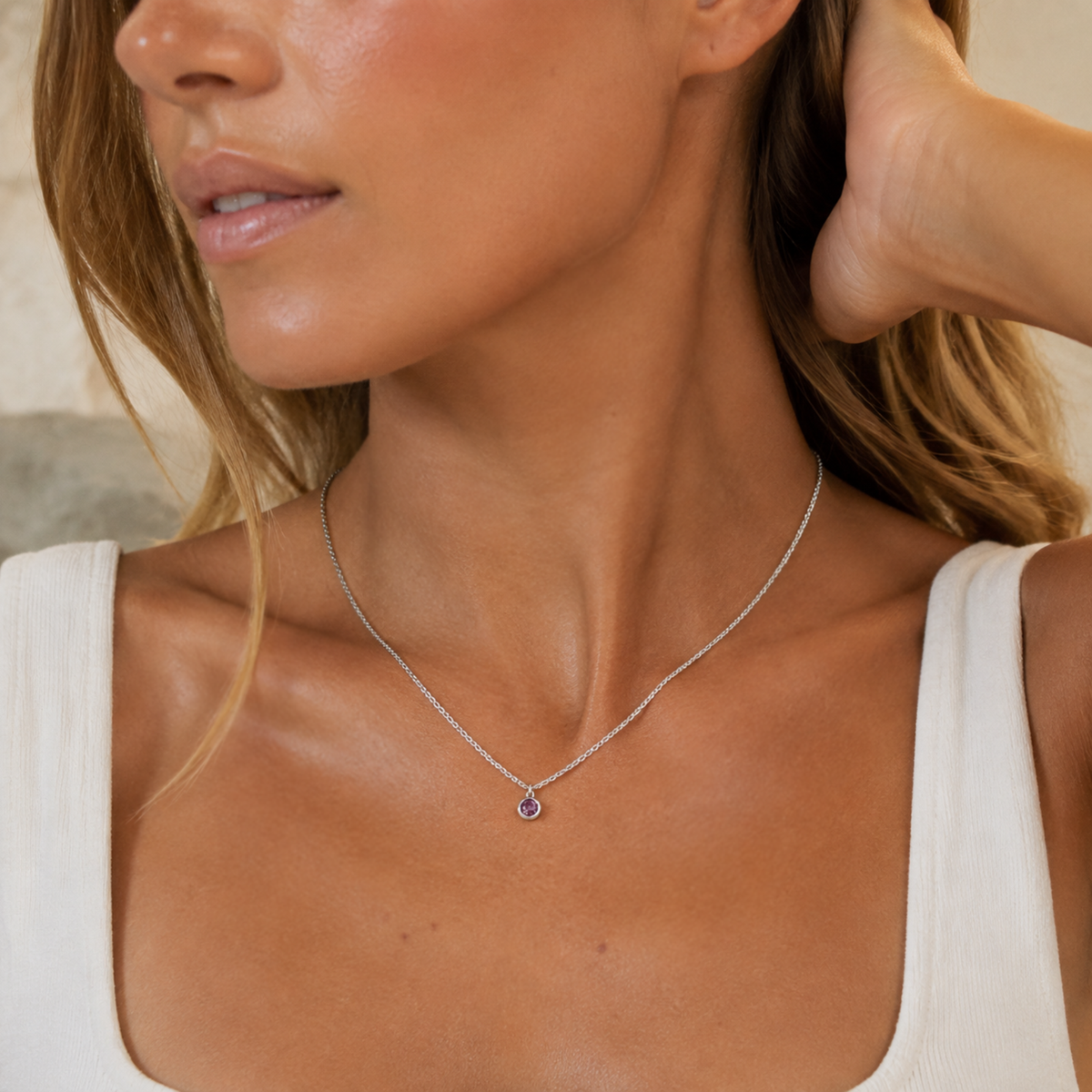 A close-up lifestyle shot of a woman wearing a delicate silver chain necklace with a small, round purple gemstone pendant.