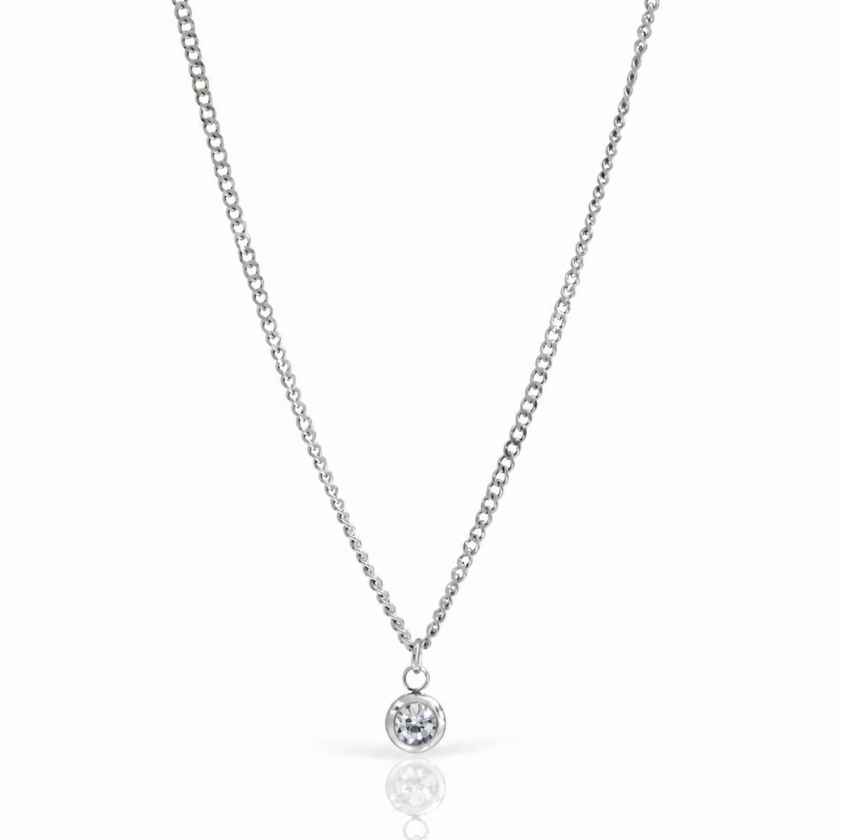 A delicate silver chain necklace with a small round bezel-set clear gemstone pendant, displayed on a clean white background with a soft reflection below.