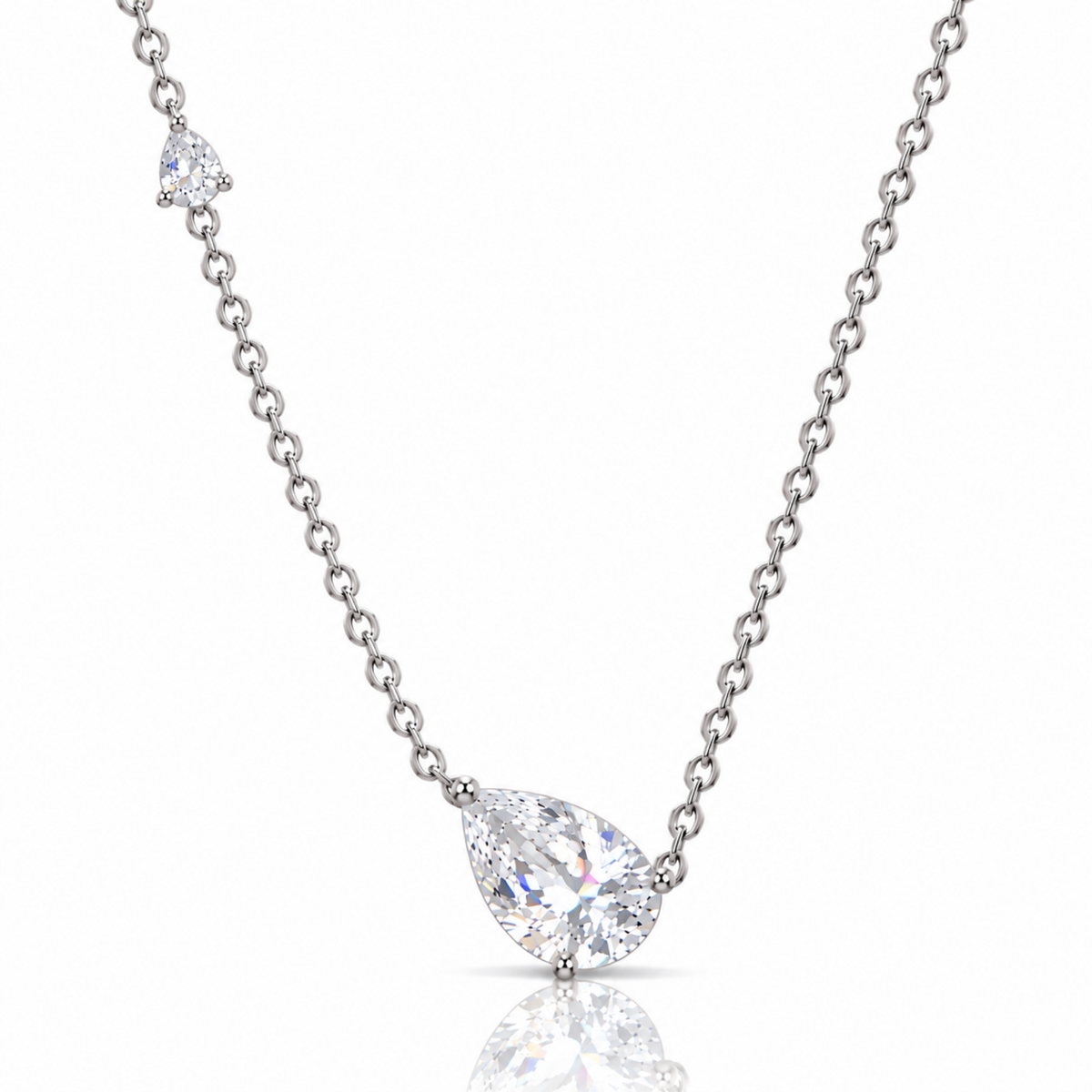 A silver-tone chain necklace featuring a pear-cut clear gemstone pendant and a smaller matching gemstone accent on the chain, set against a clean white background with a soft reflection below.
