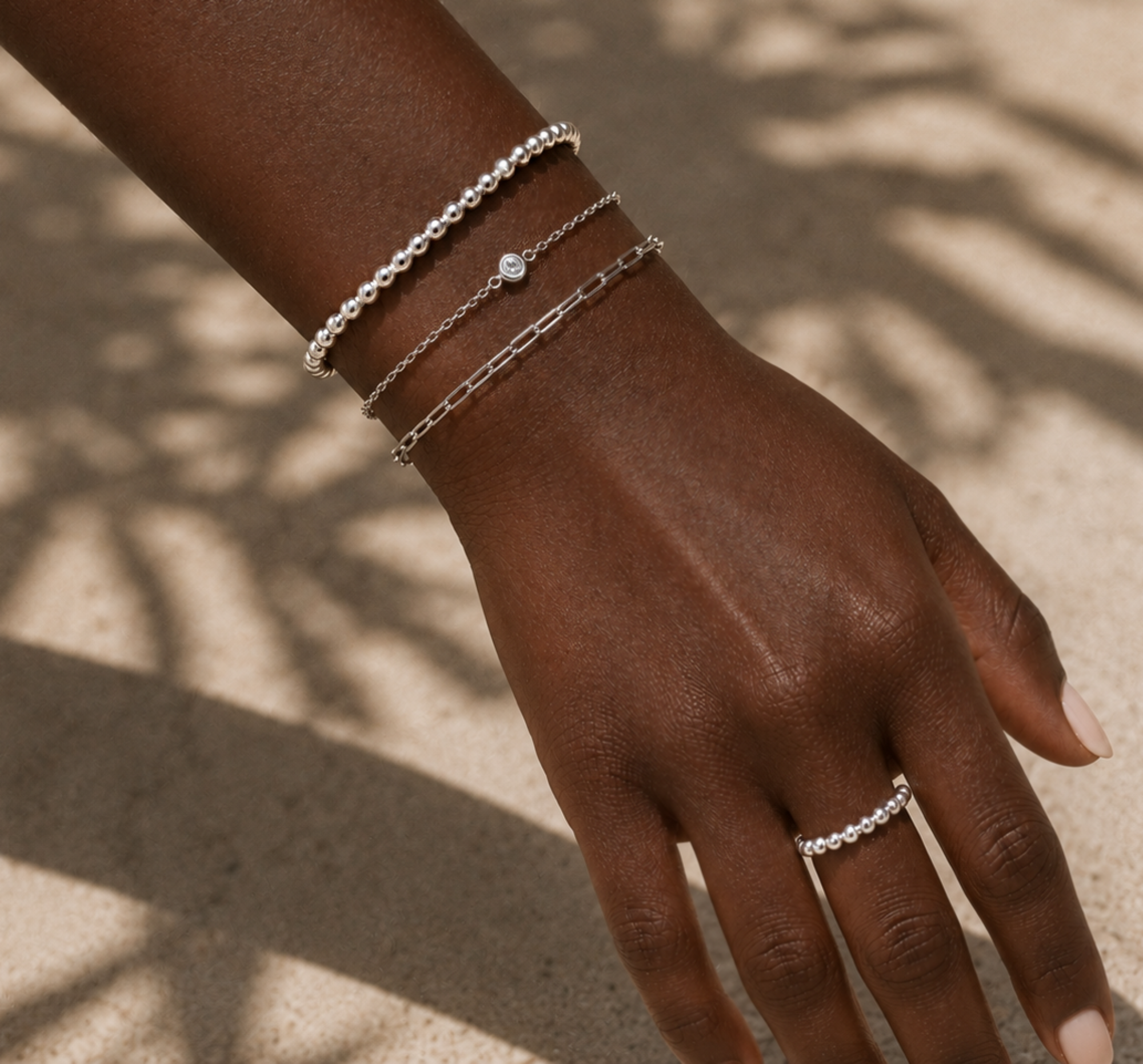 Hand wearing multiple silver bracelets and a ring on a neutral background