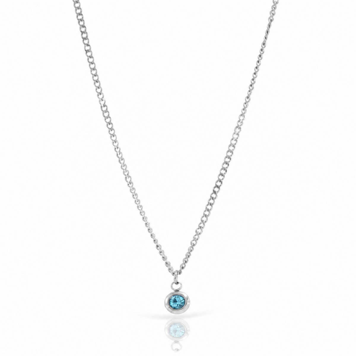 A delicate december birthstone silver chain necklace with a small oval pendant featuring a light blue gemstone, displayed on a clean white background with a soft reflection below.