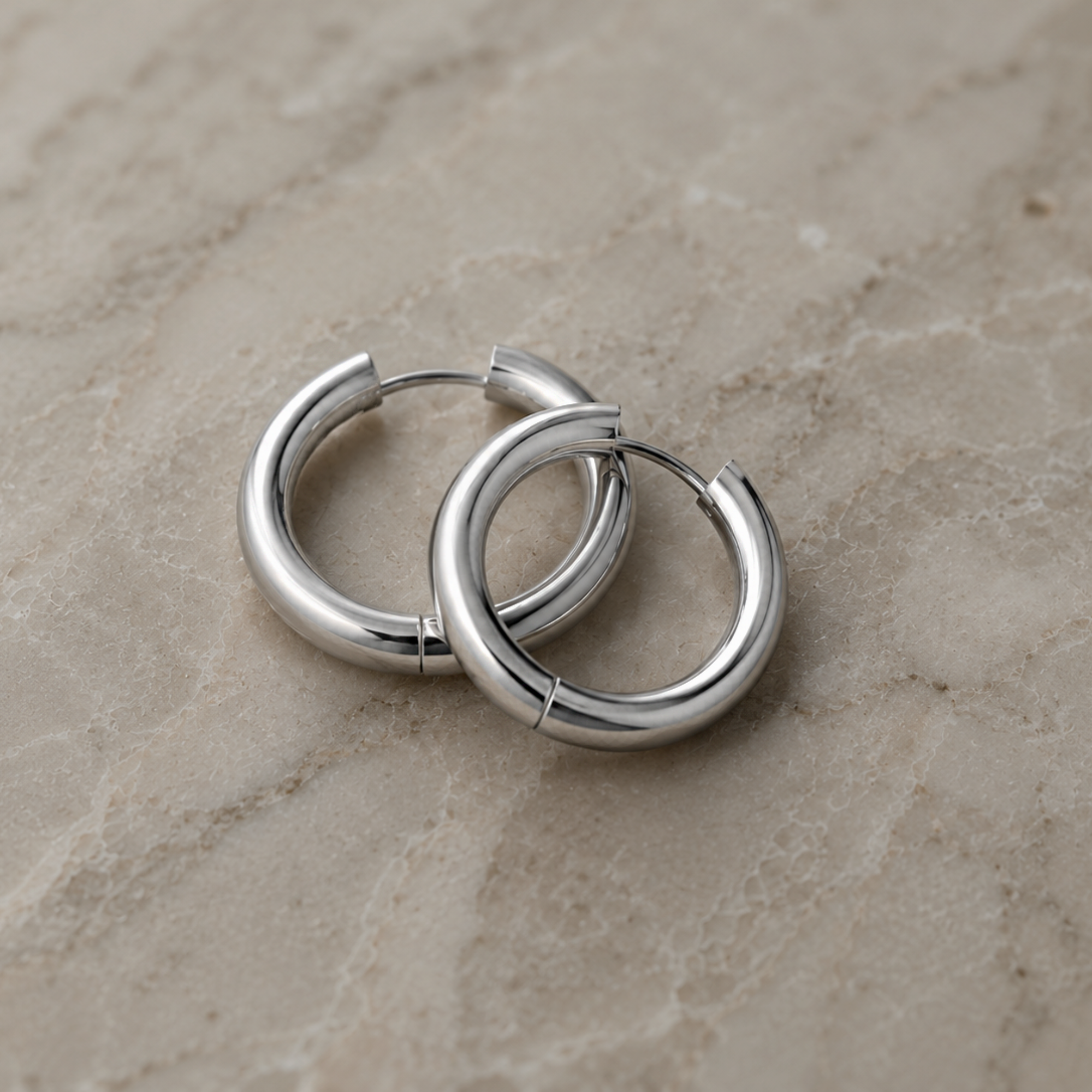 Pair of silver hoop earrings on a beige marble surface