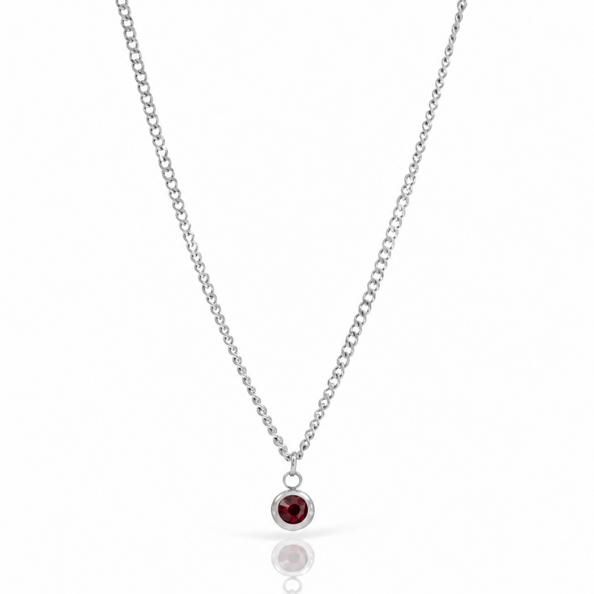 A silver chain necklace with a small bezel-set round red gemstone pendant, shown on a clean white background with a soft reflection below.